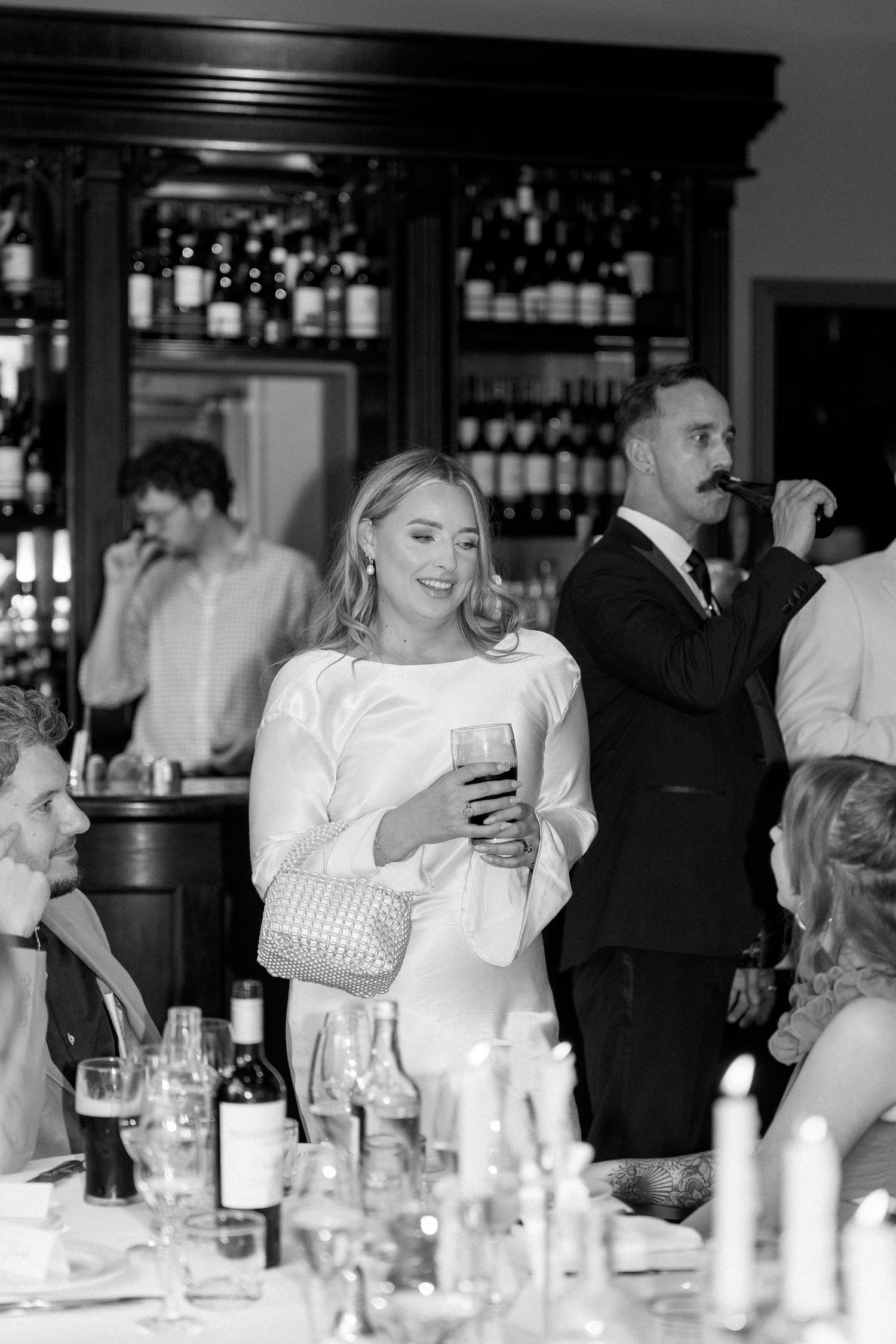 A black and white reception scene with guests enjoying drinks at a bar.