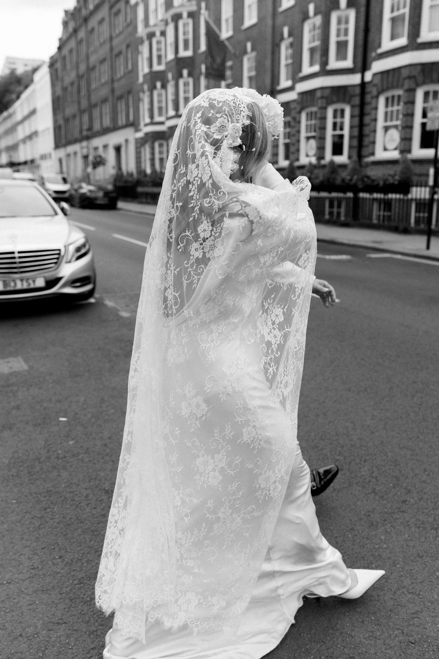A flowing white lace wedding dress captured in motion on a city street.