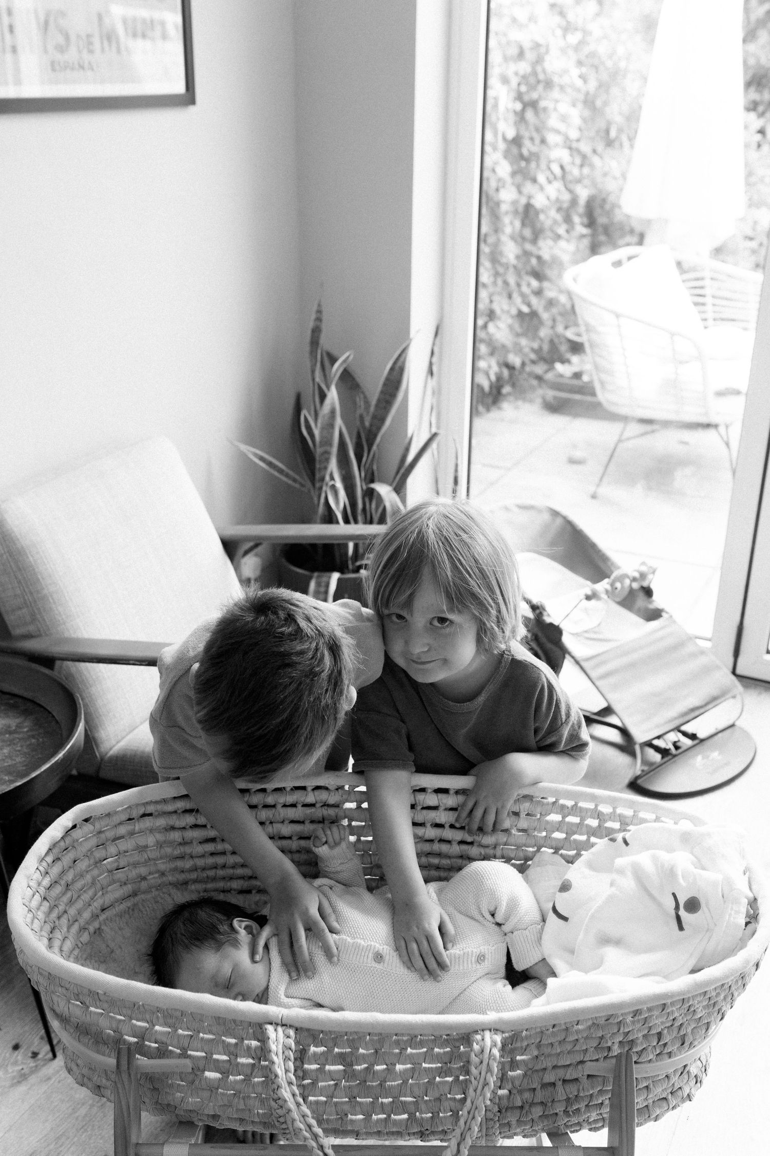 Black and white photos showing playful interaction between parent and child in a woven basket by a window.