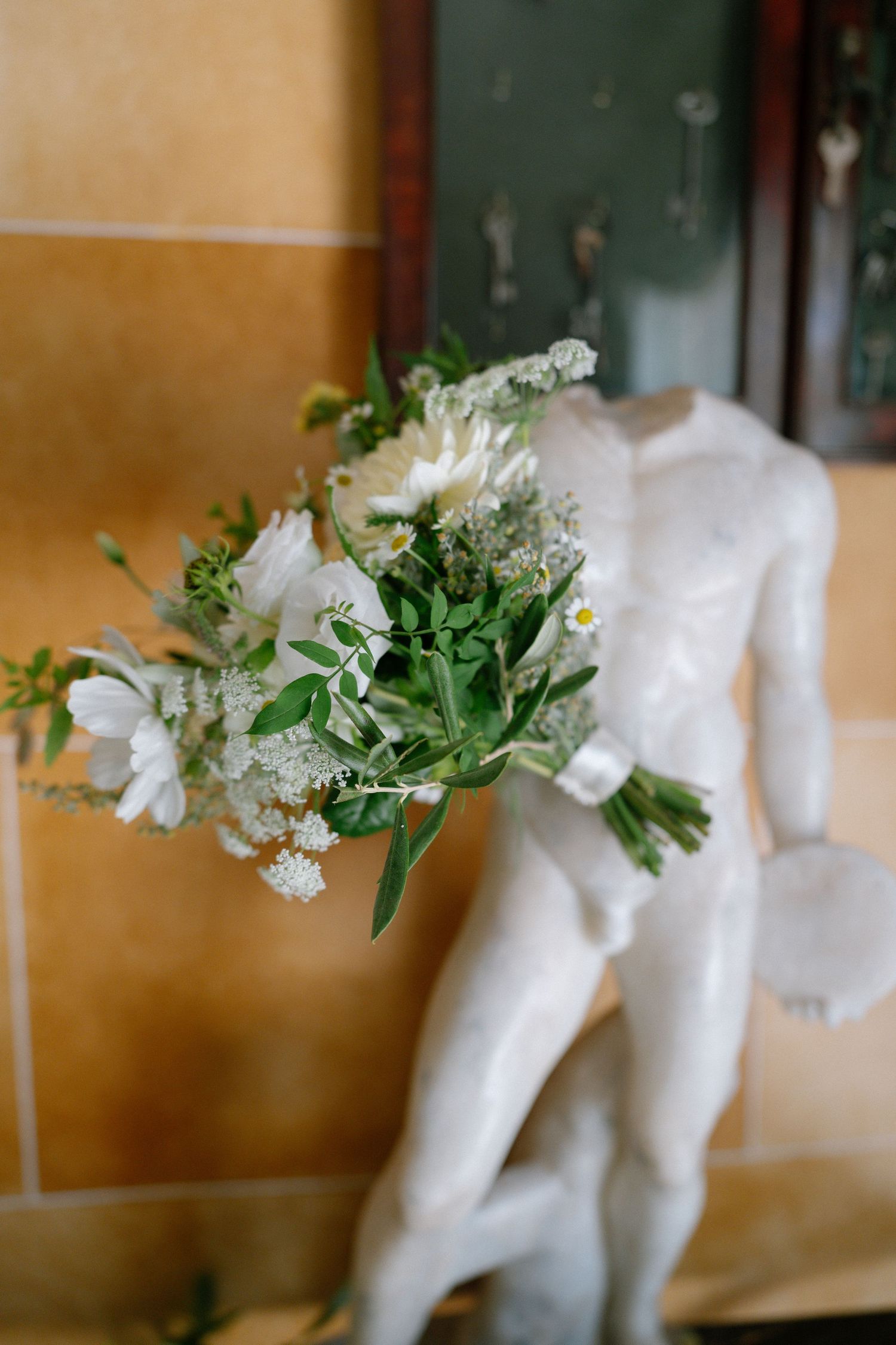 White floral bouquet with greenery against a warm-toned wall.