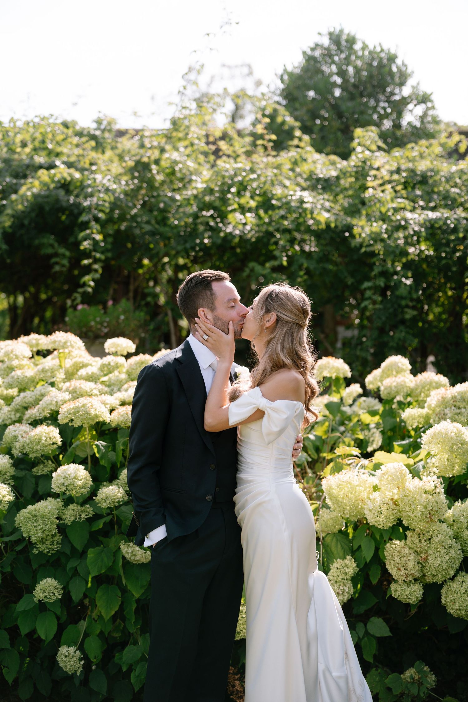 A couple shares intimate kisses against a backdrop of cream hydrangea blooms.