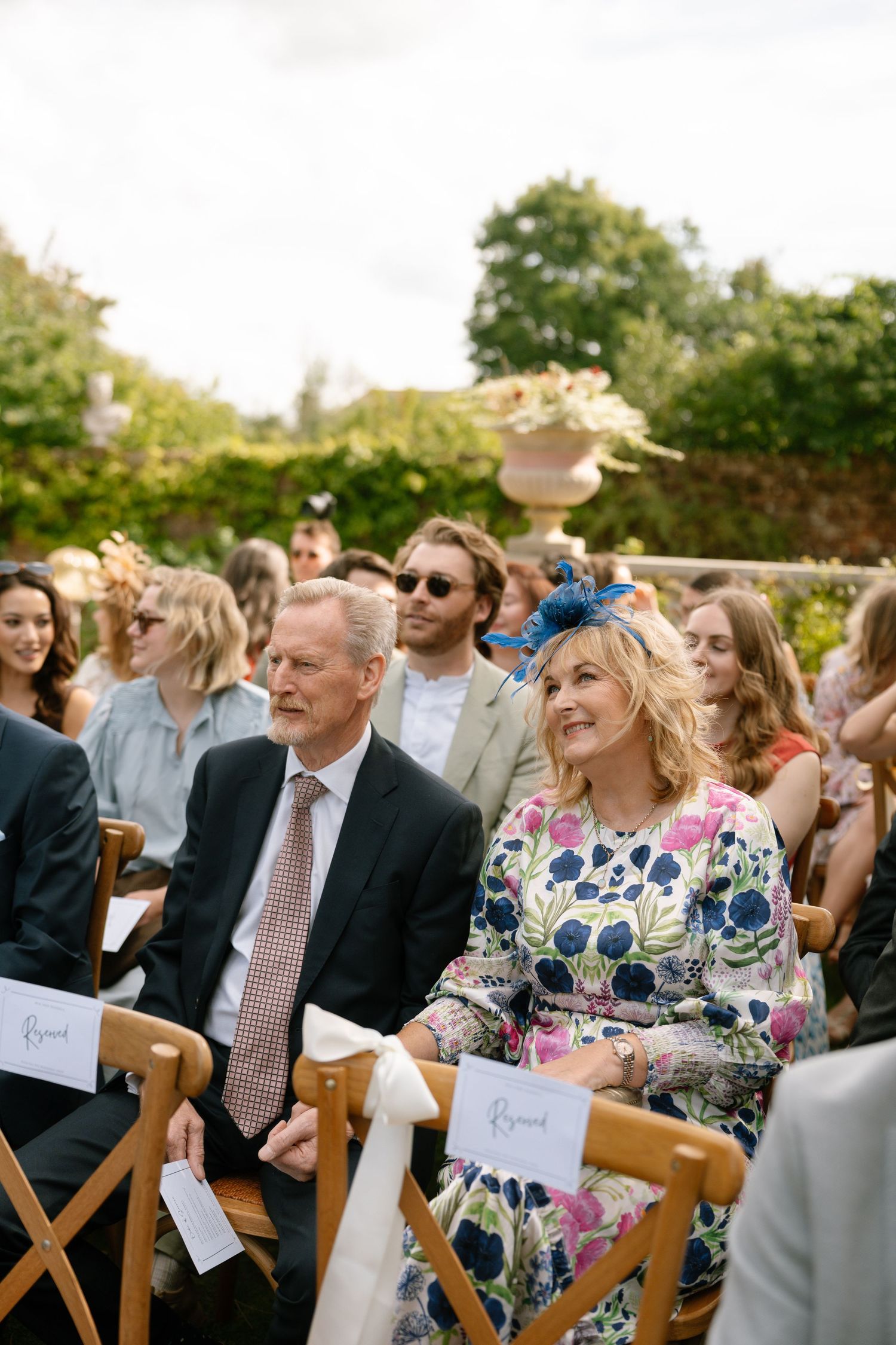 Wedding guests seated in wooden chairs at an outdoor garden ceremony.
