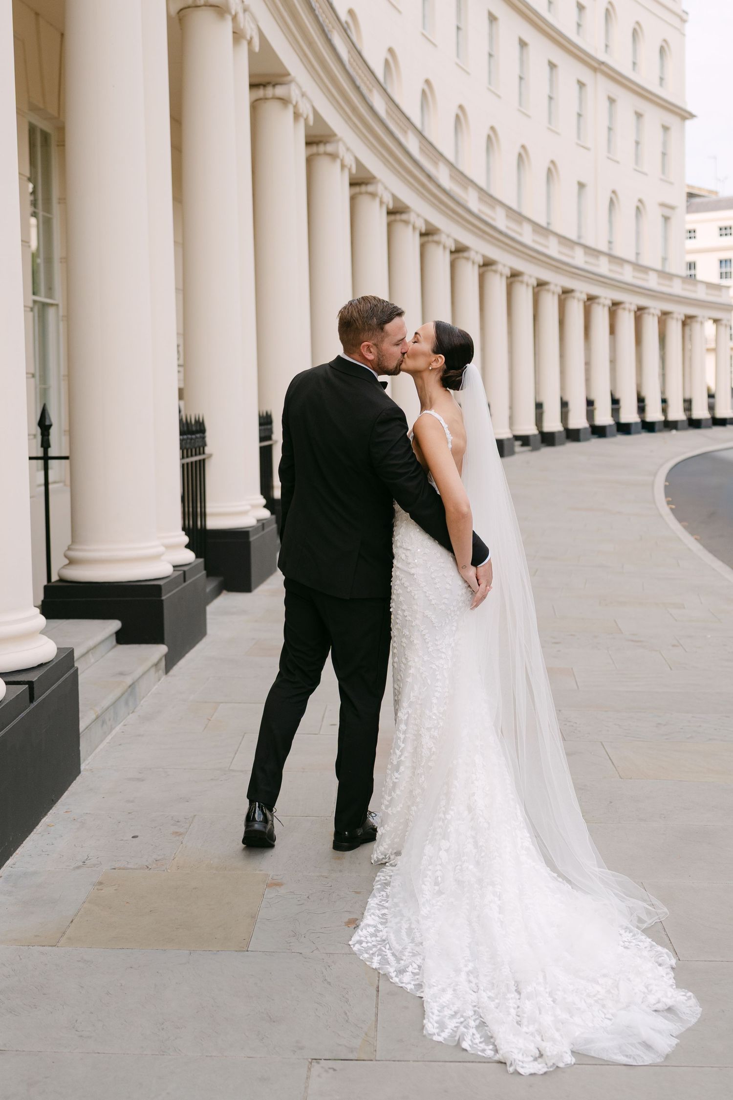 A tender wedding moment between newlyweds against classic white architecture.