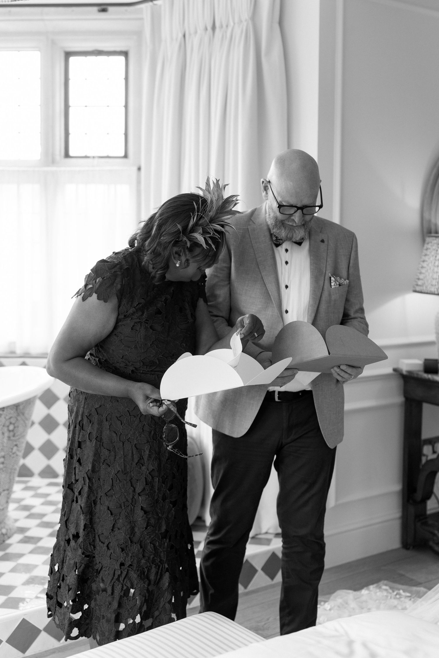 Black and white photo of wedding guests reviewing documents in a checkered tile bathroom.
