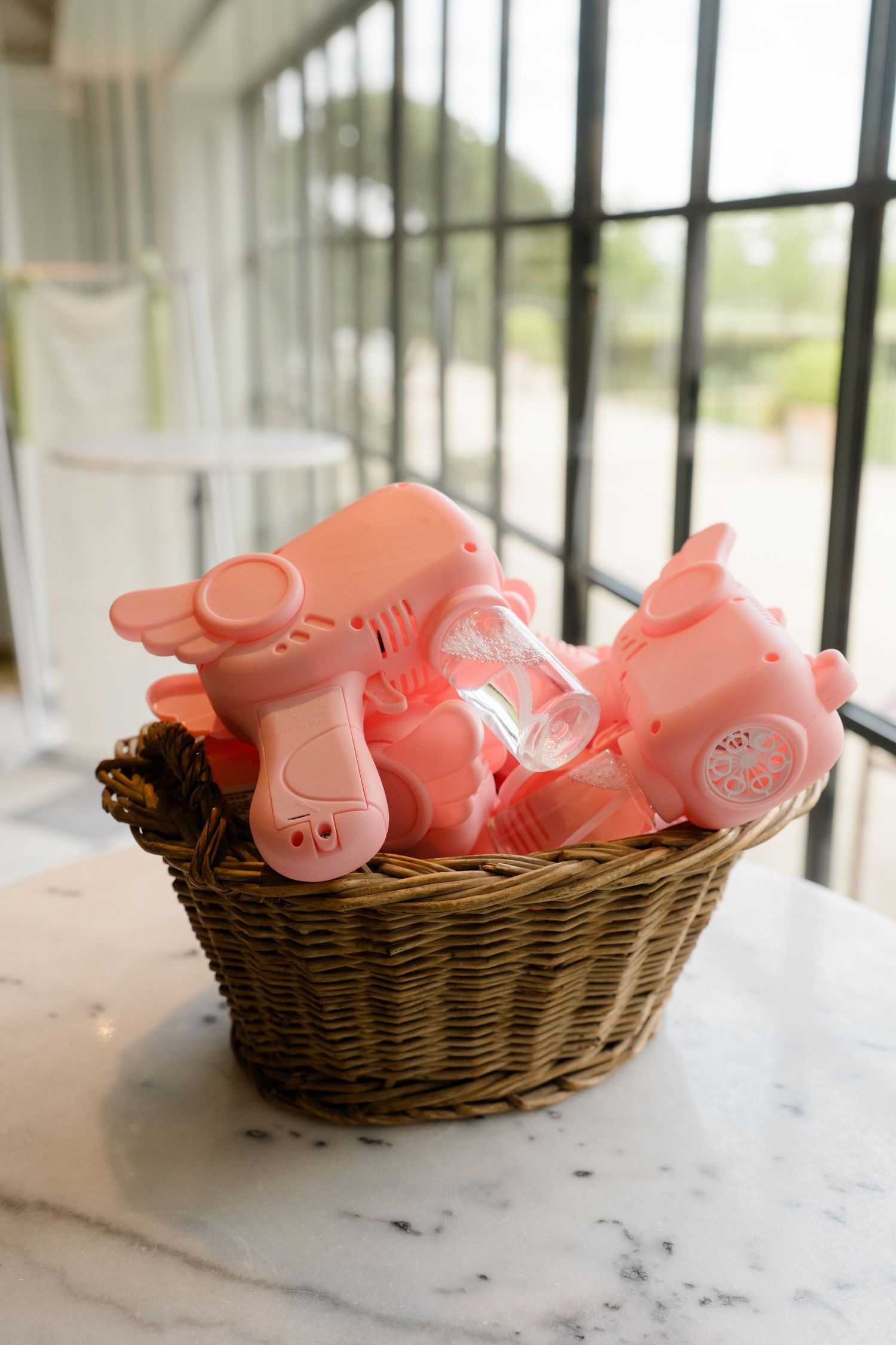 Wicker basket filled with pink bubble blowers as fun wedding favors displayed on a marble surface.