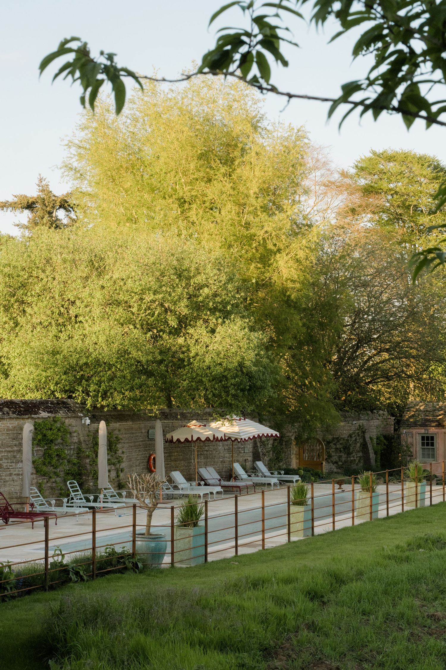 Serene outdoor pool area with lounge chairs and umbrella surrounded by lush green trees at wedding venue.