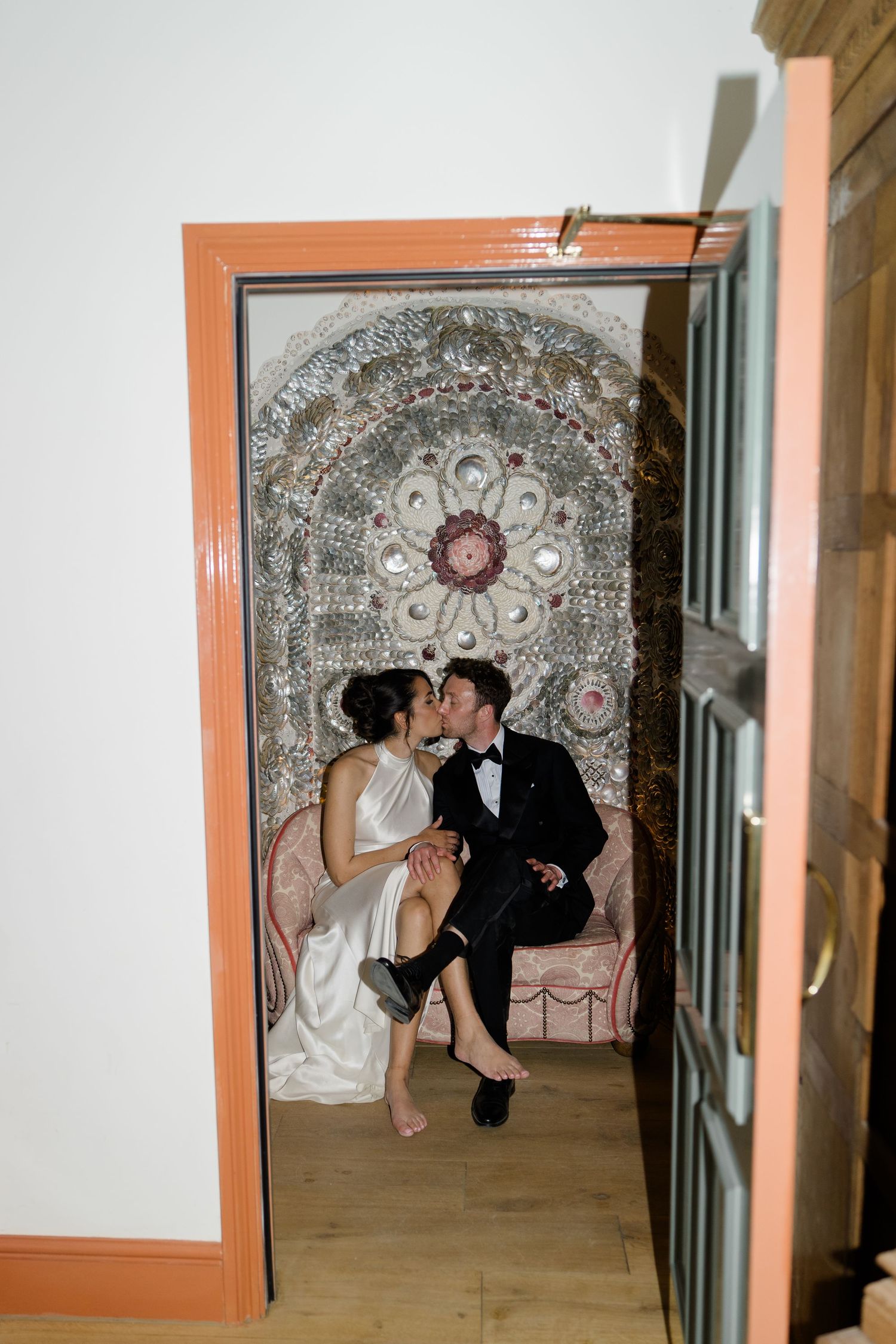 Bride and groom steal a romantic kiss in an ornate shell grotto alcove inside their wedding venue.