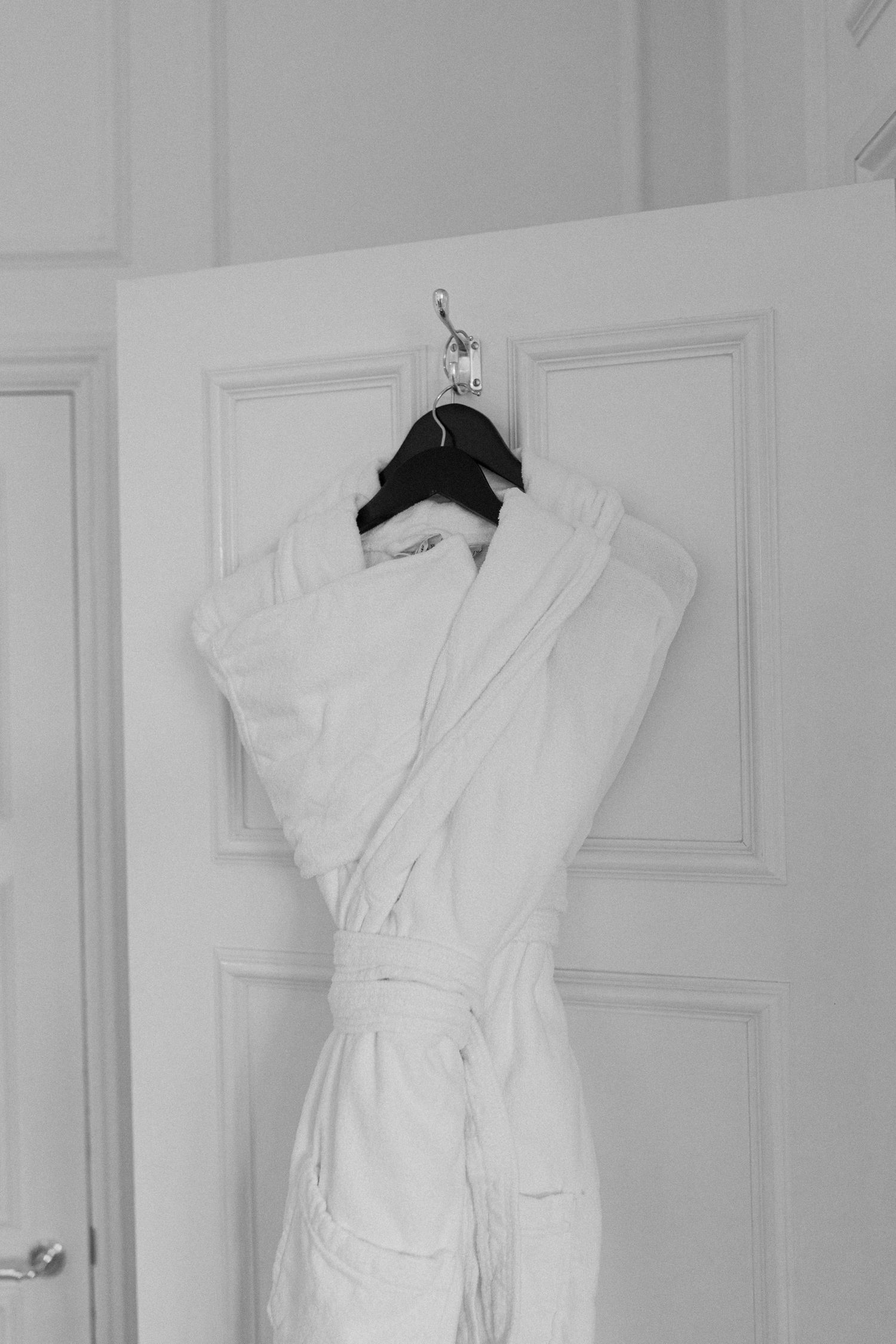 White terrycloth robe hanging on a door hook on a black hanger for wedding preparations.