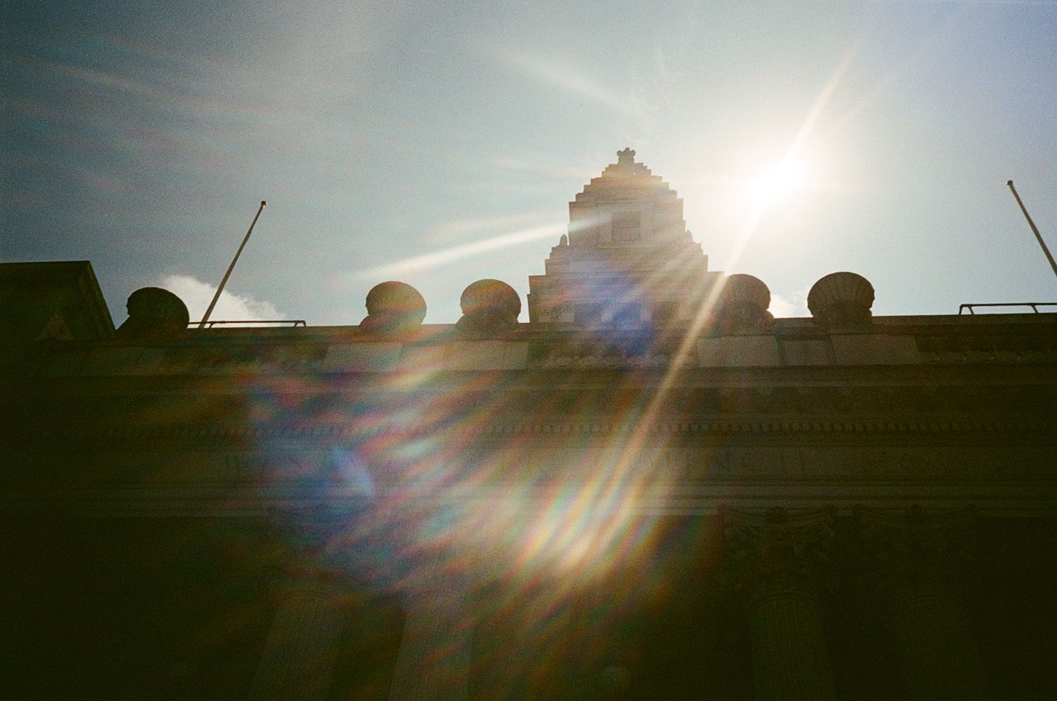 Silhouette of ornate temple architecture against bright sun with dramatic lens flare in blue sky.