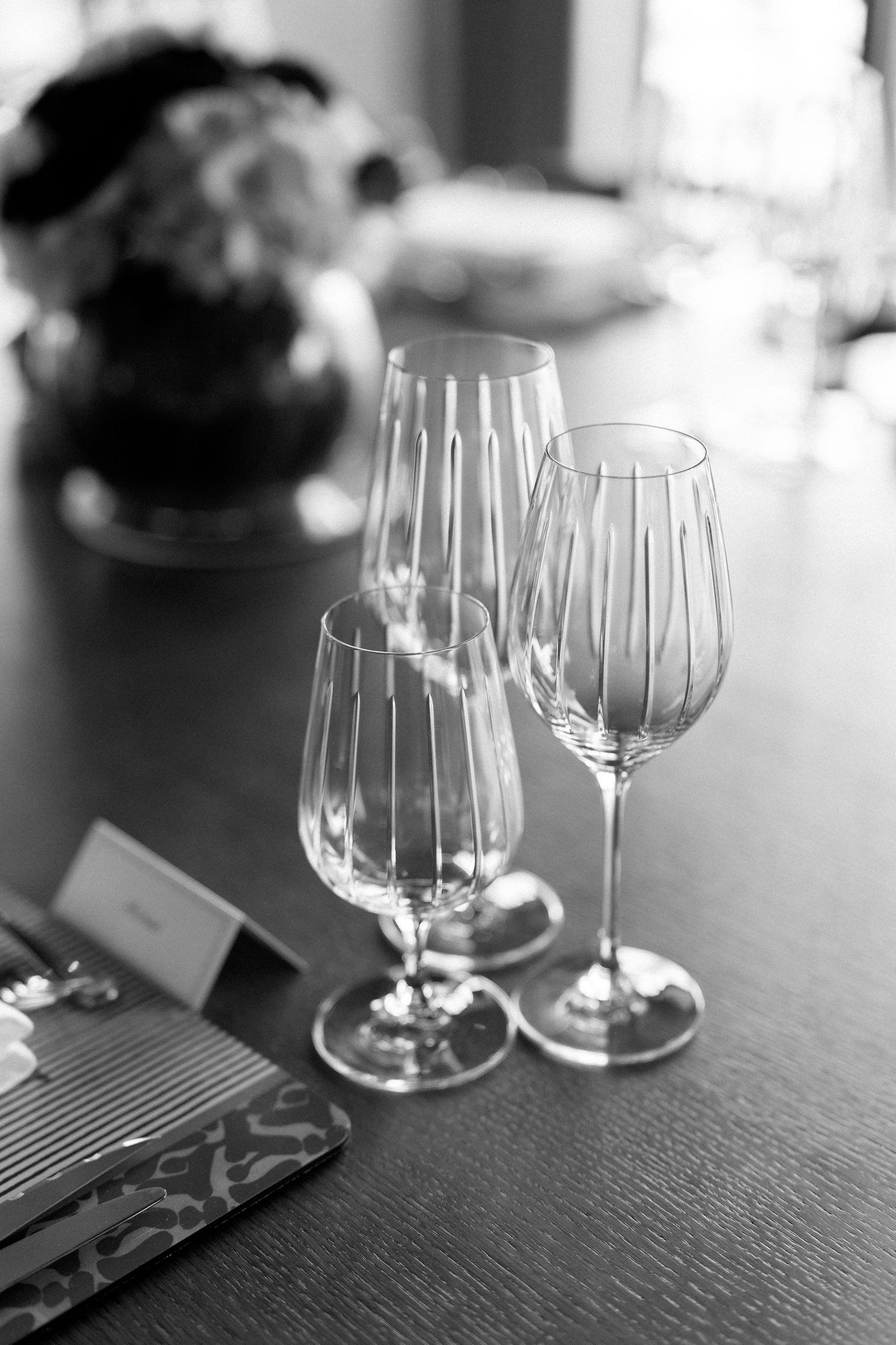 Elegant black and white photo of three empty crystal wine glasses arranged on a wooden table at a wedding reception.