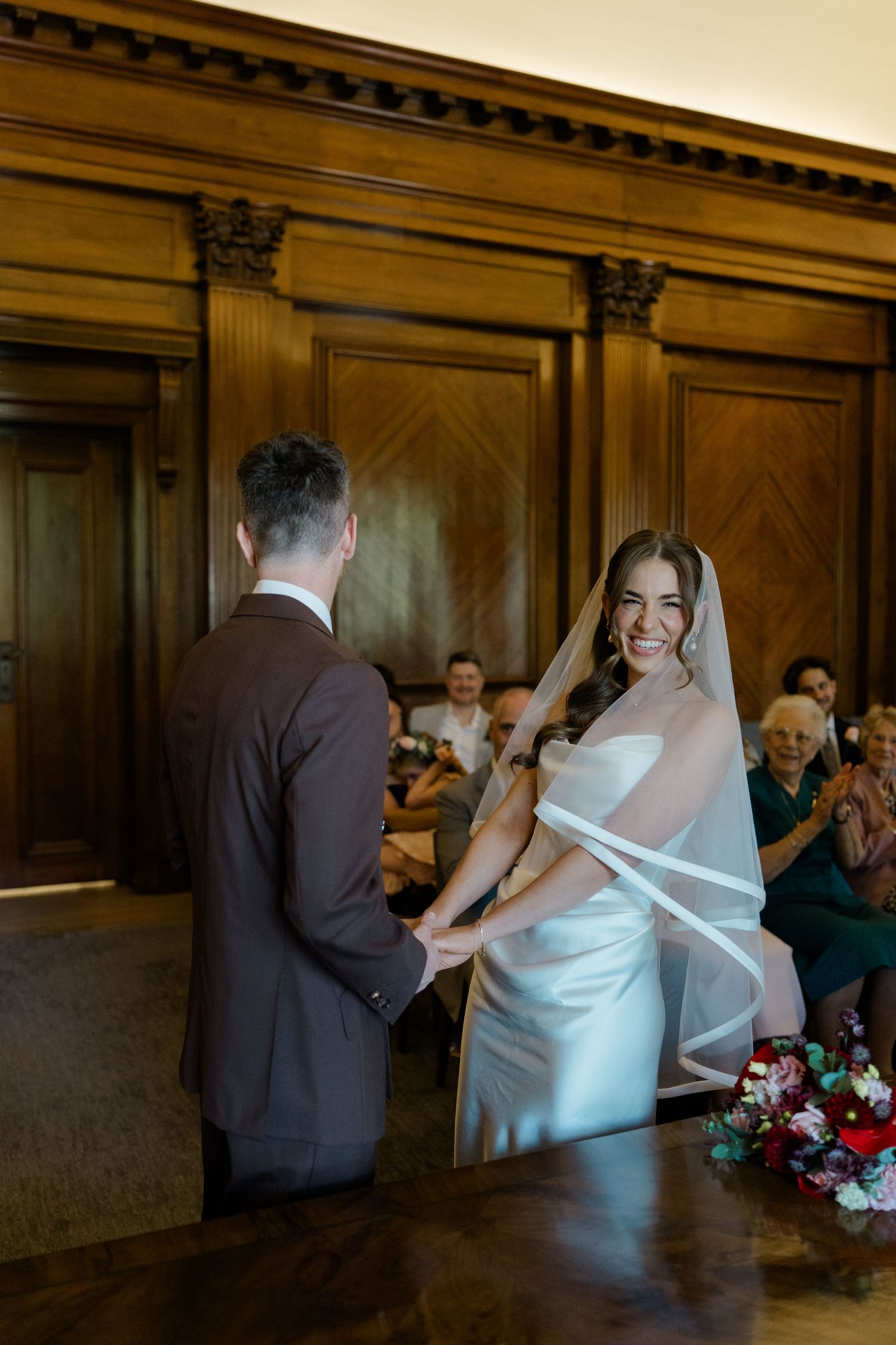 Bride and groom holding hands at altar during wedding ceremony with guests seated in background.