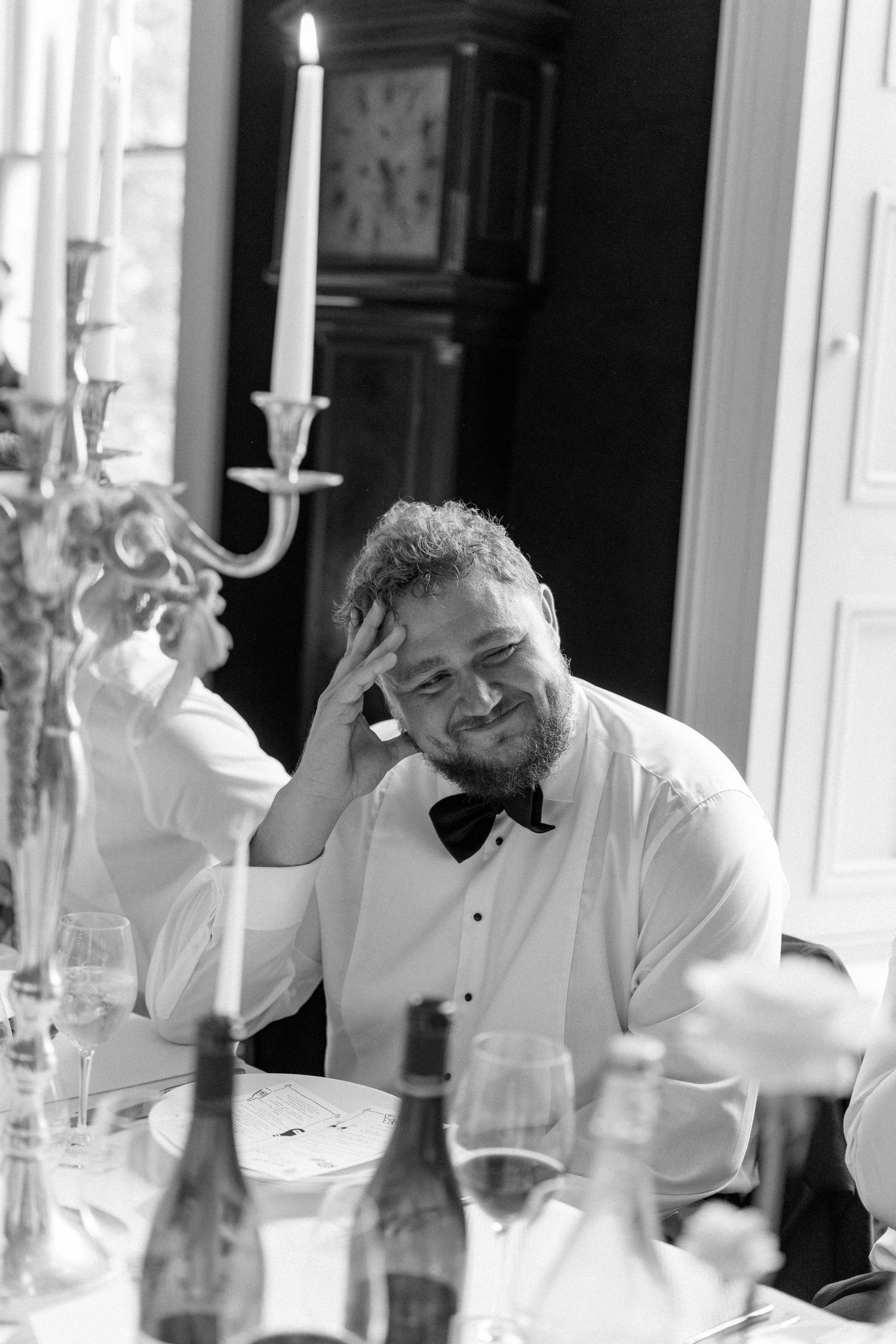 Black and white photo of a smiling wedding guest relaxing at a candlelit reception dinner table.