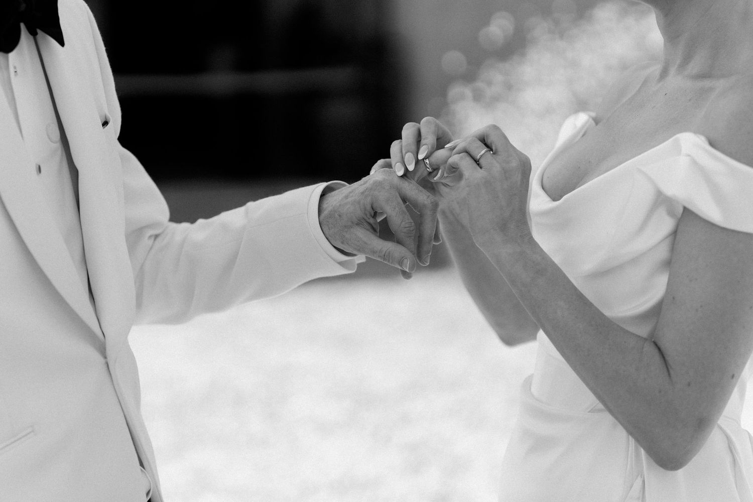 Close-up black and white photo of a groom placing a wedding ring on the bride's finger during ceremony.