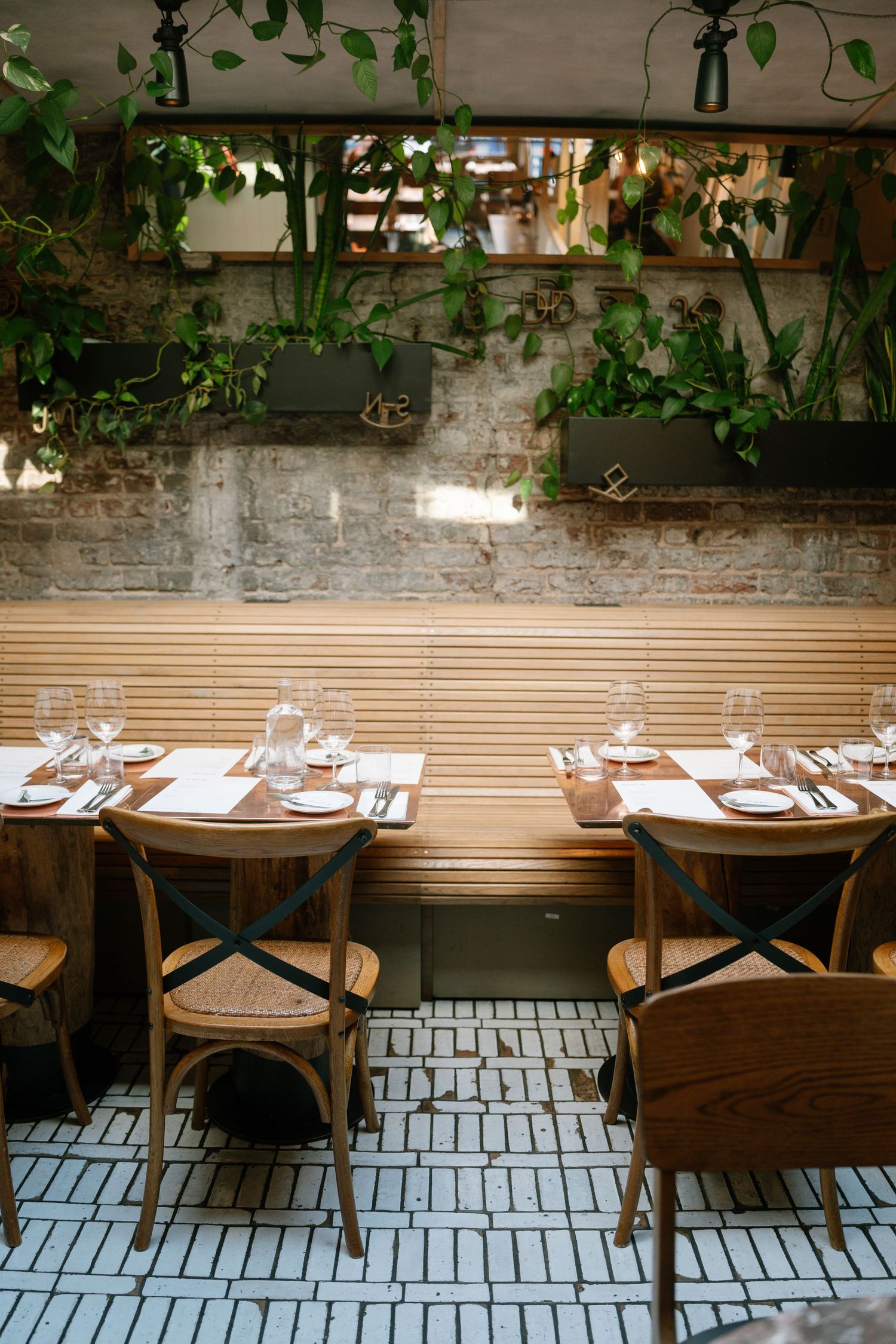 Restaurant interior with wooden tables and chairs set against exposed brick walls with hanging plants.
