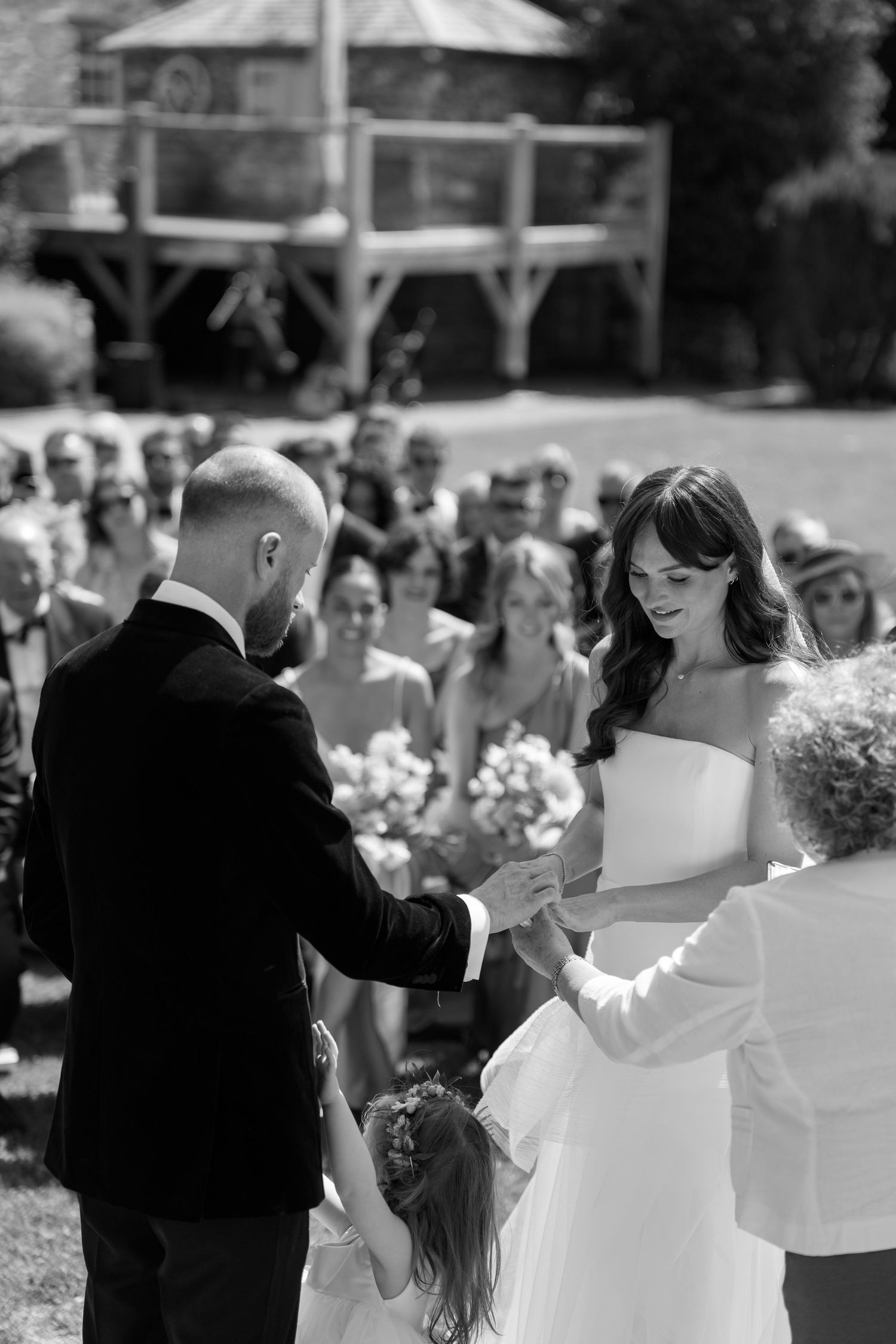 Wedding party dancing outdoors on a sunny day with stone building in background.