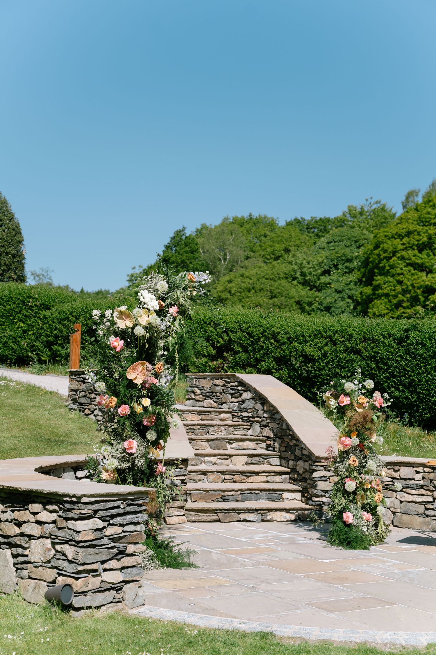 Stone pathway decorated with floral arrangements leading to outdoor ceremony space.