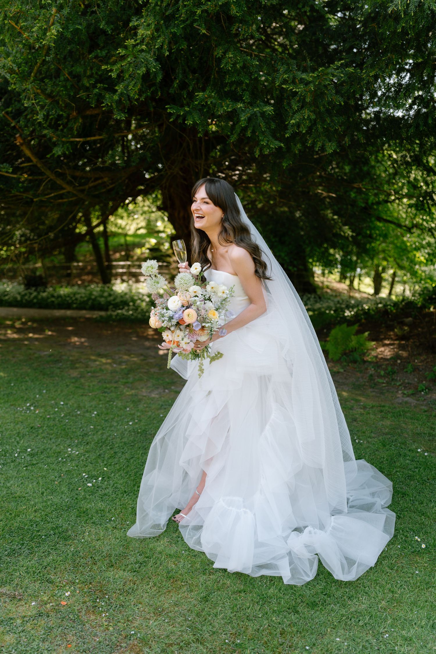Elegant white wedding dress spreads across green grass during outdoor bridal shoot.