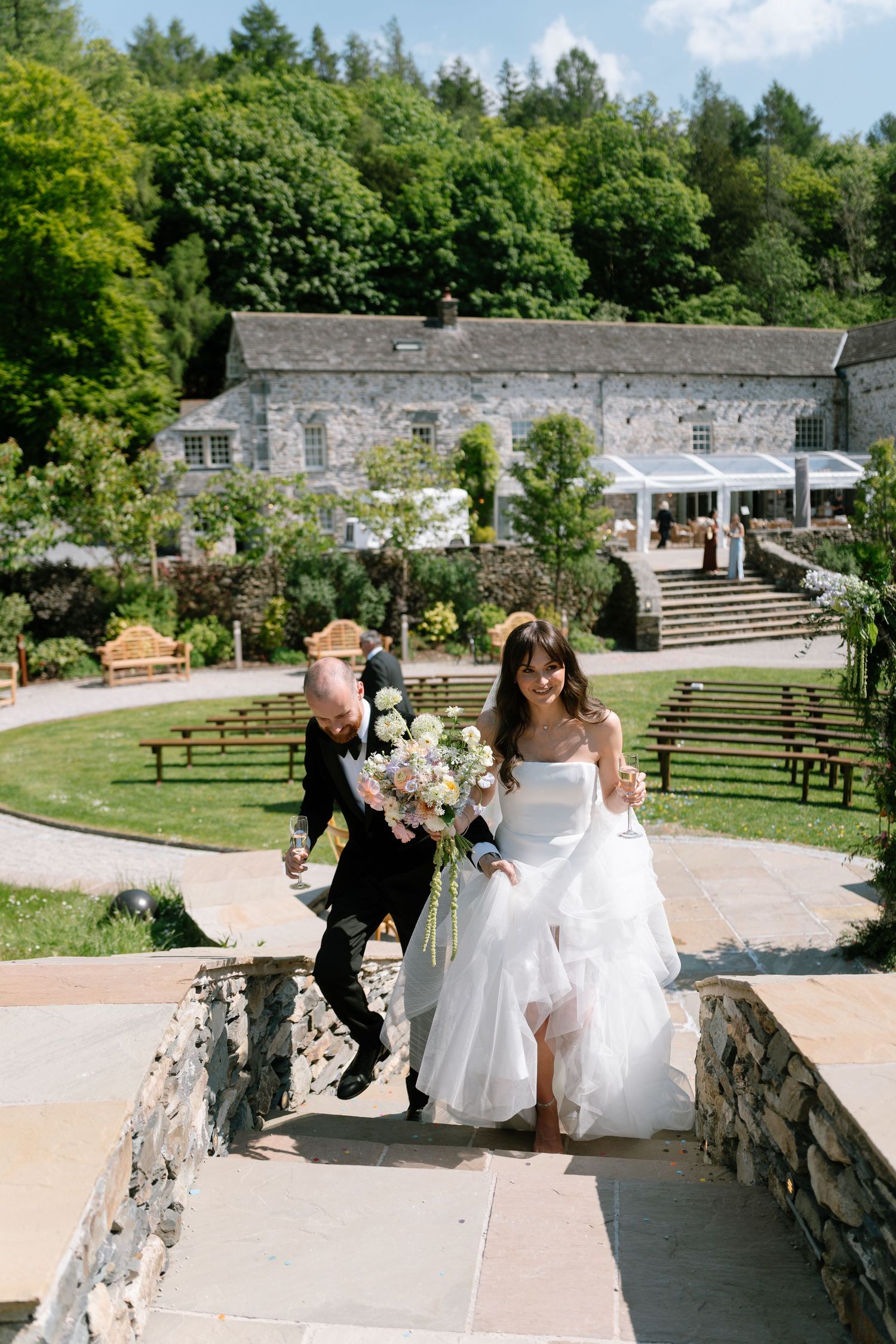 Wedding celebration in a lush garden with stone walls and steps in the background.