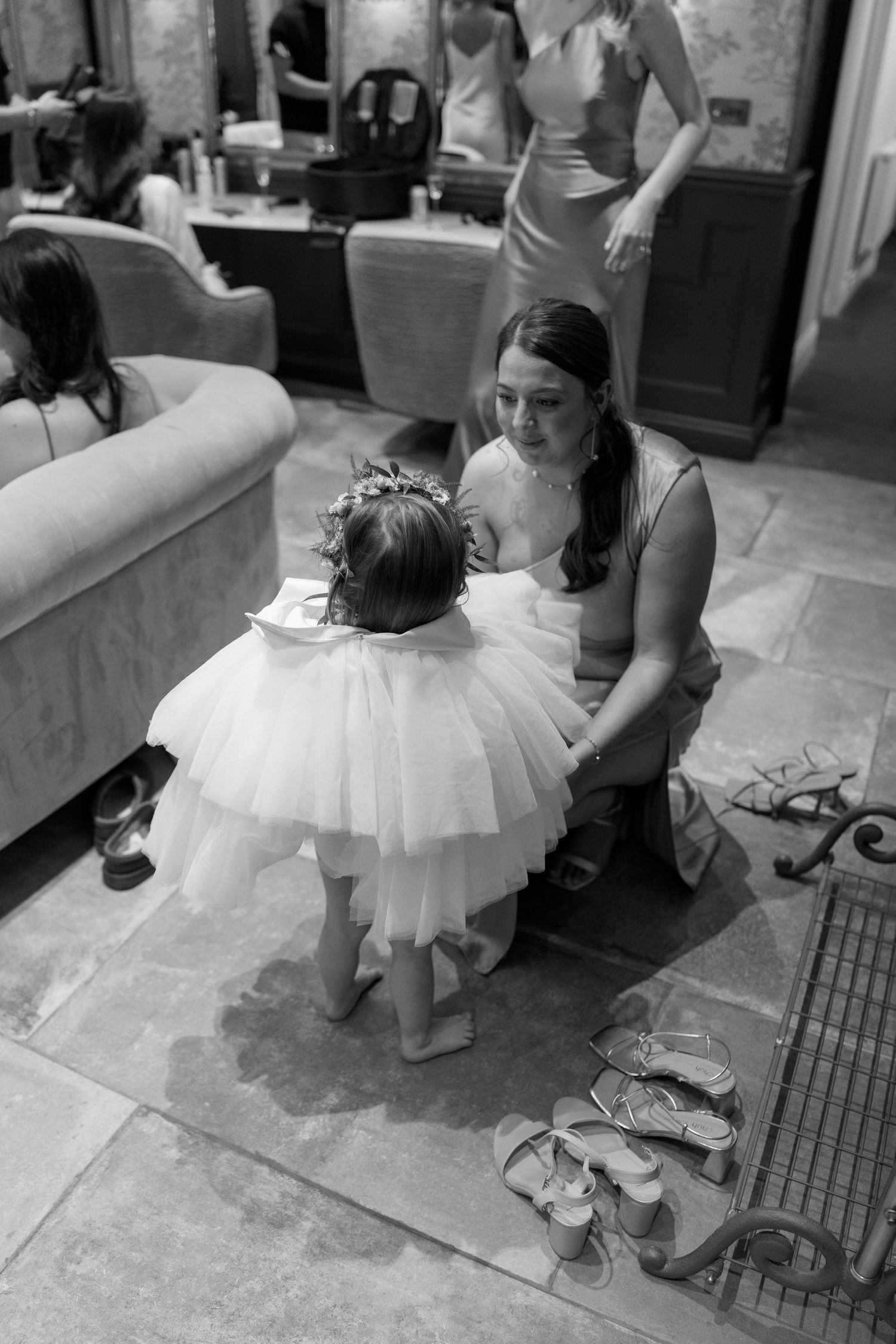 Young flower girl in white tulle dress gets ready with help in a dressing room.