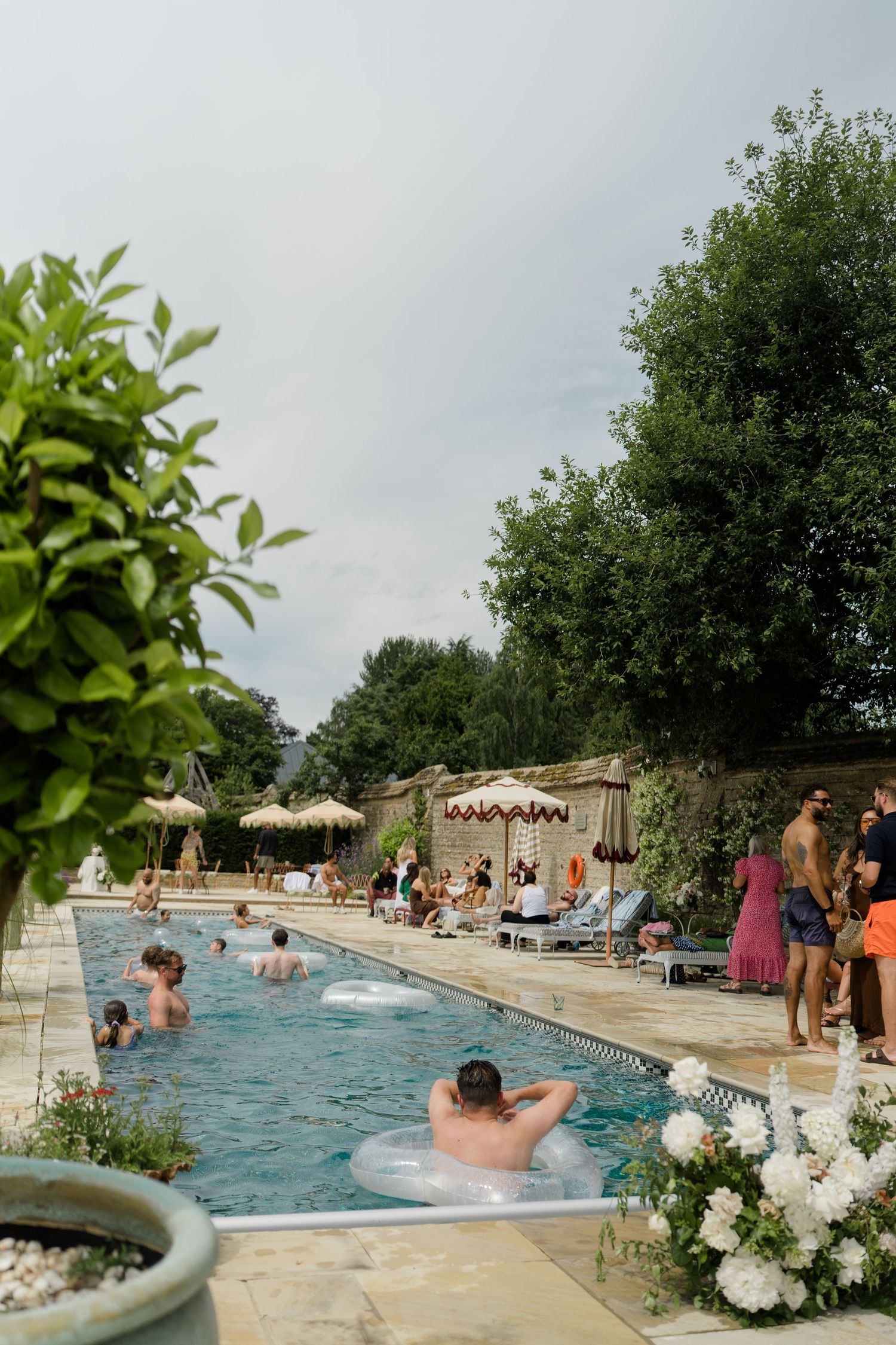 Wedding guests enjoying outdoor pool party with floats, lounge chairs, and lush garden surroundings.