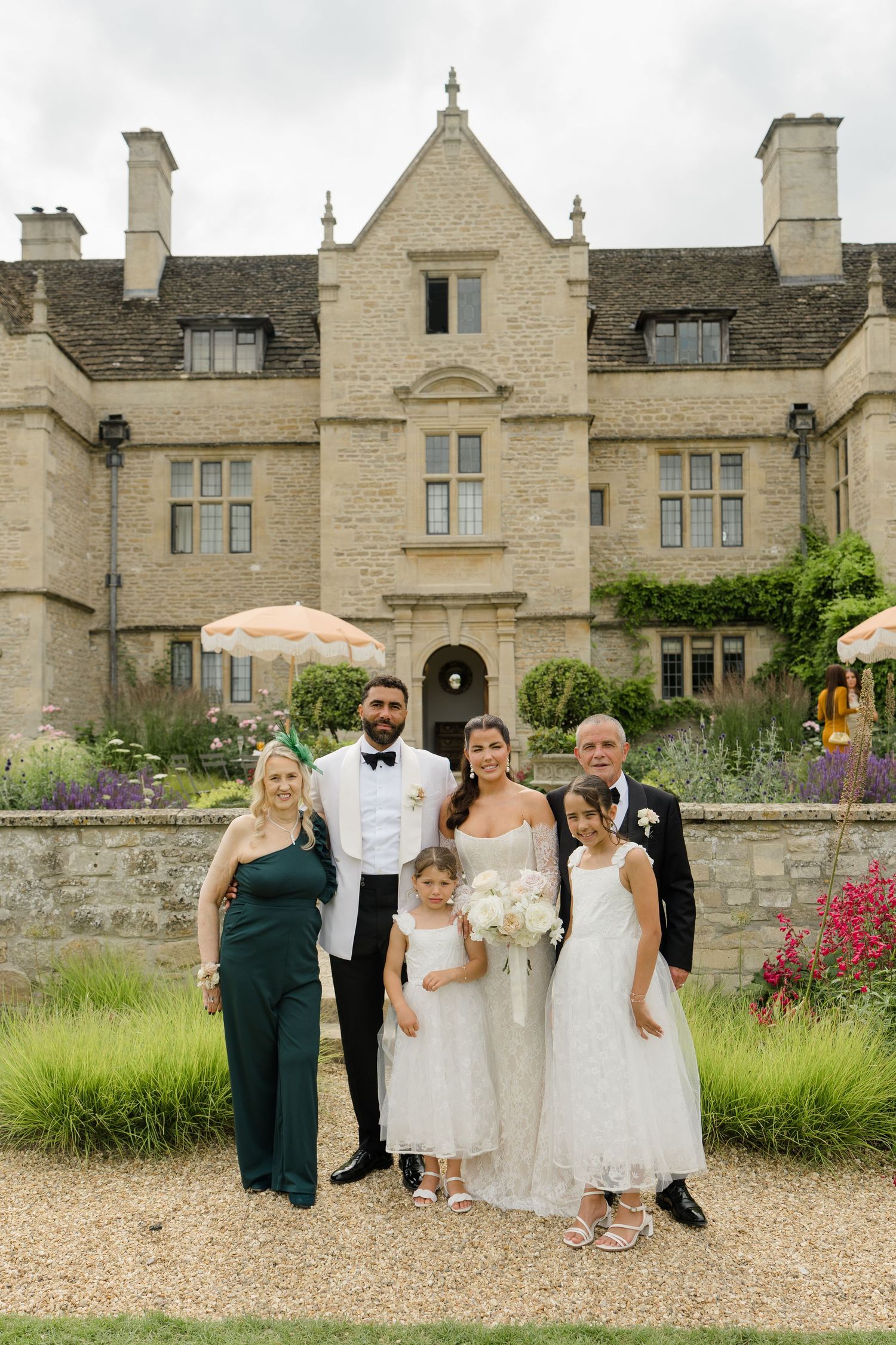 Wedding party family portrait with bride, groom, flower girls, and parents before stone manor.