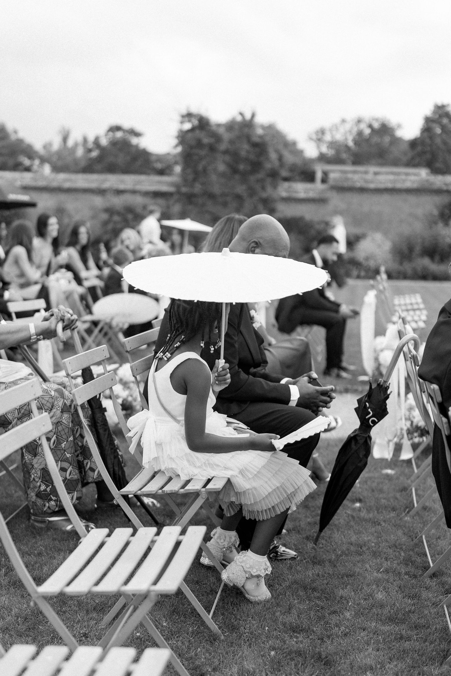 Young girl sitting with adult under white parasol umbrella at outdoor wedding ceremony.