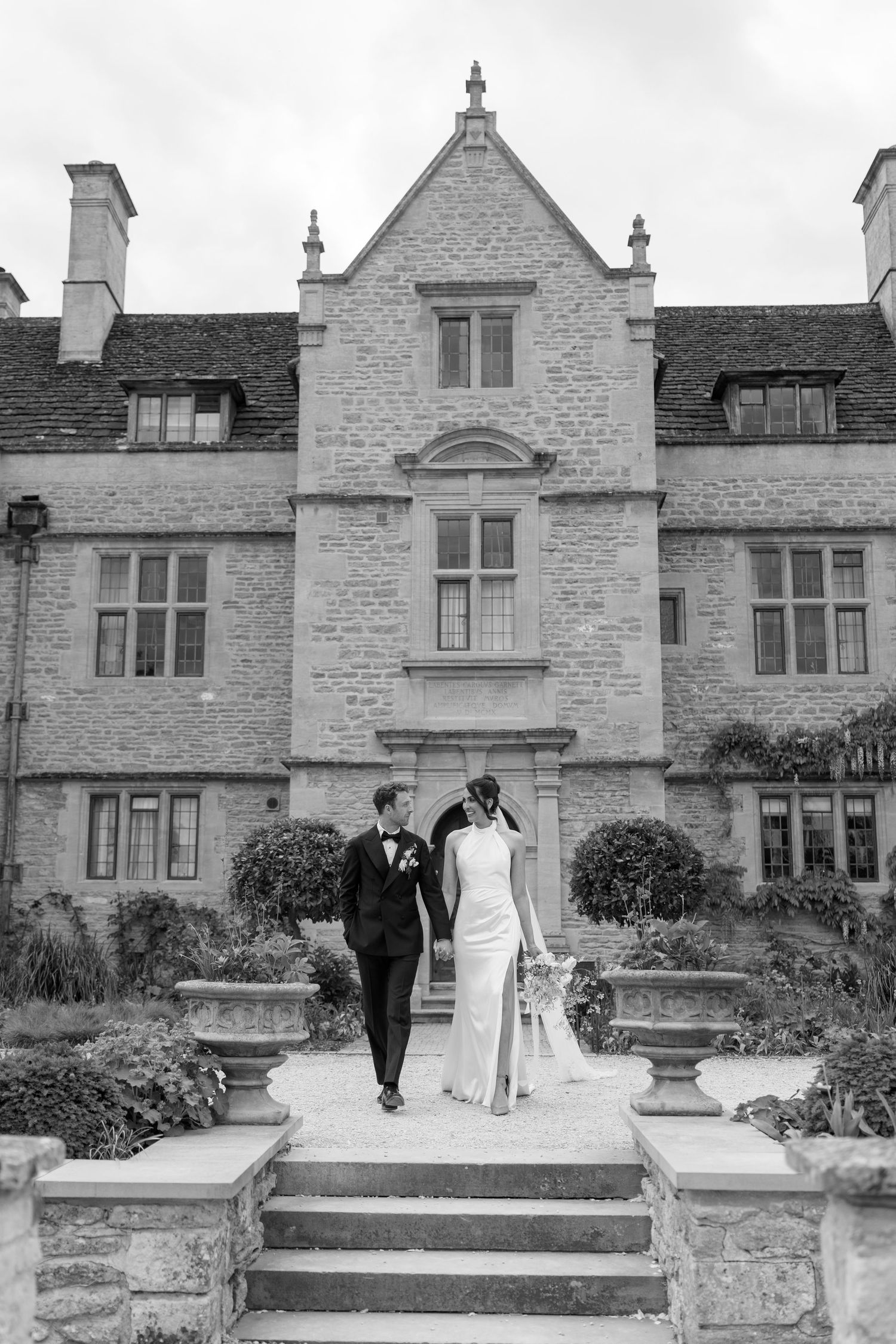 Black and white photo of bride and groom descending steps of grand stone manor house.