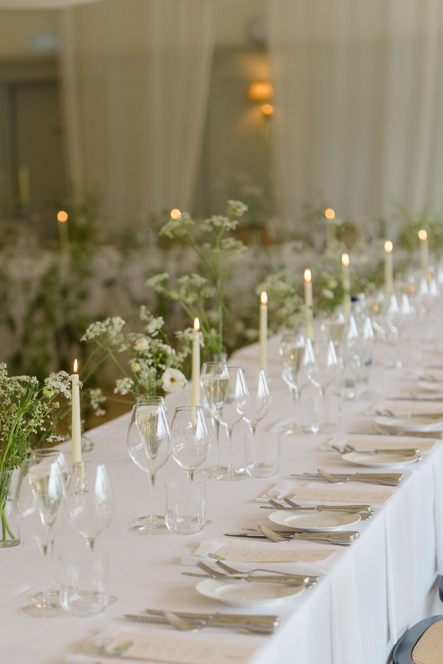 Long elegantly set wedding reception table with candles, glassware, and delicate floral arrangements.