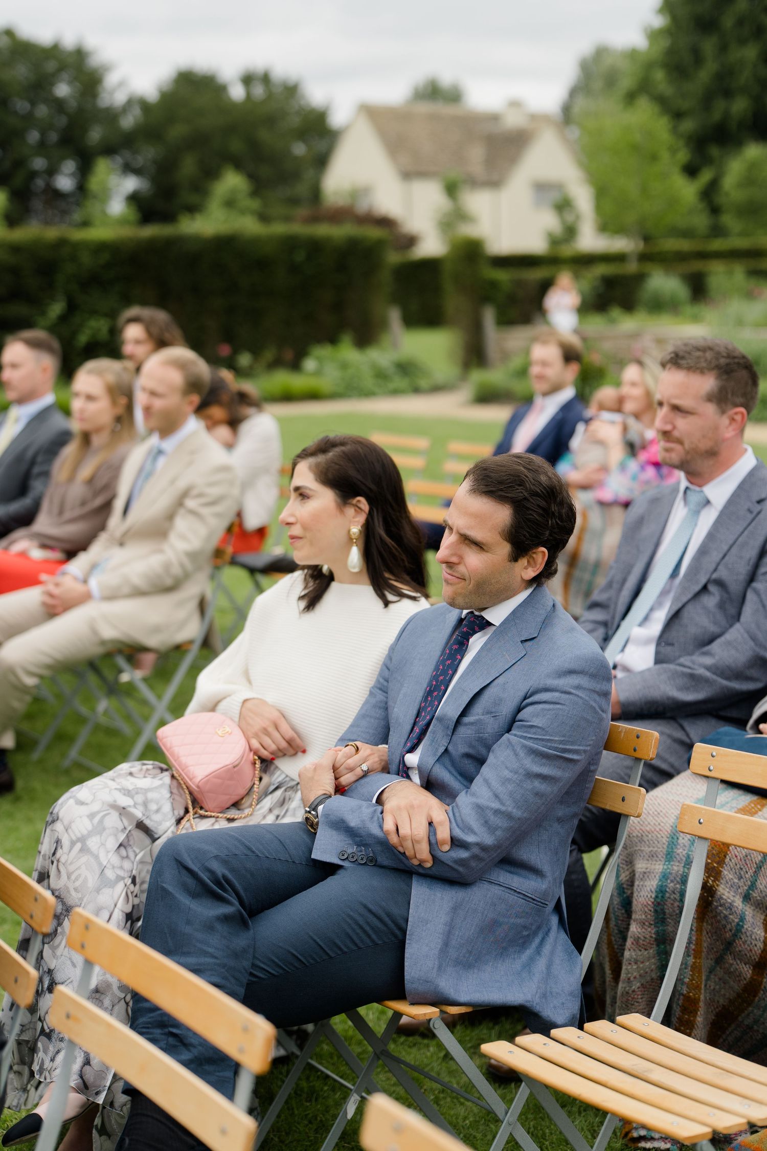 Wedding guests seated on wooden chairs during an outdoor garden ceremony at a manor.