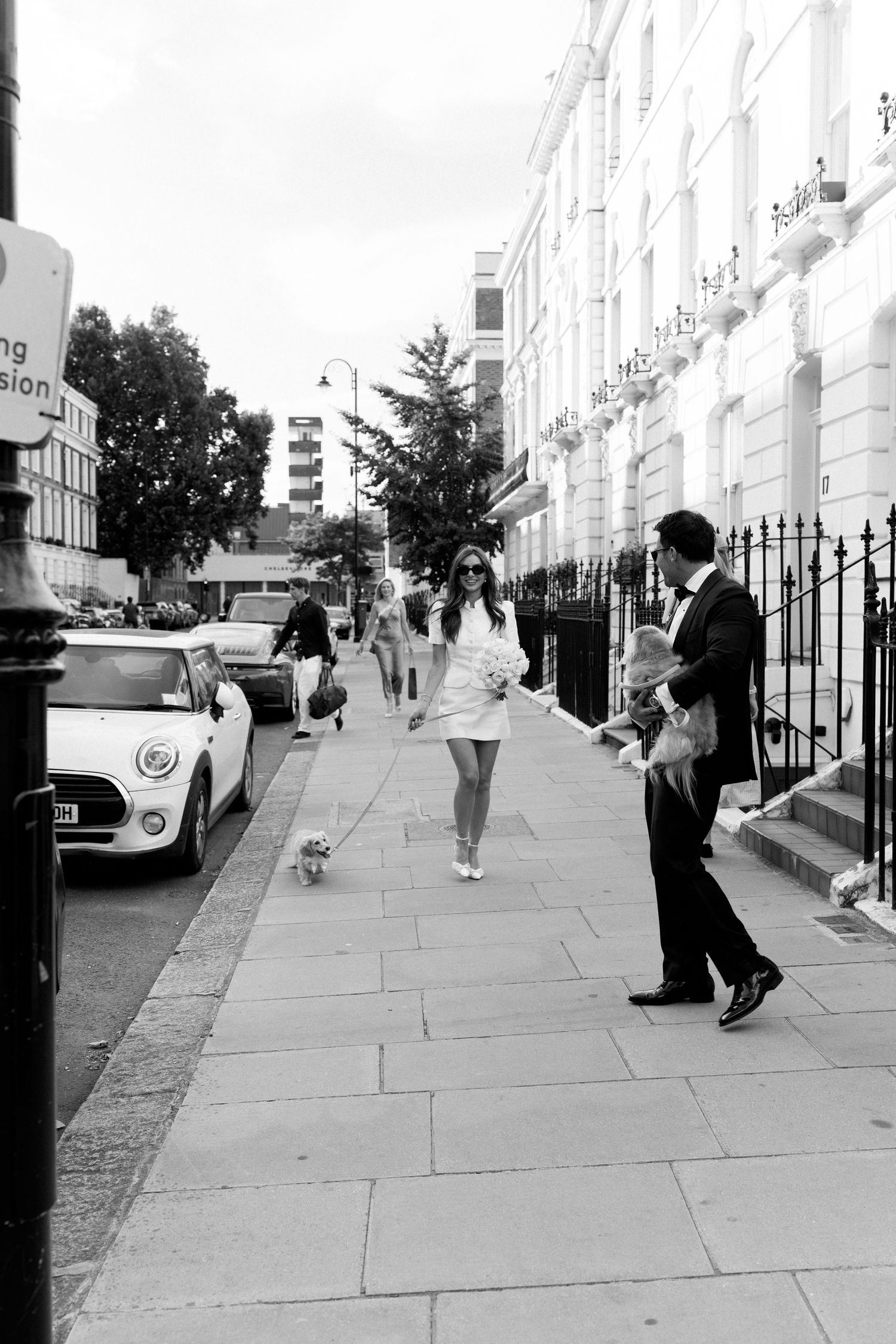 Bride and groom stroll along elegant London street with small dog after civil wedding ceremony.