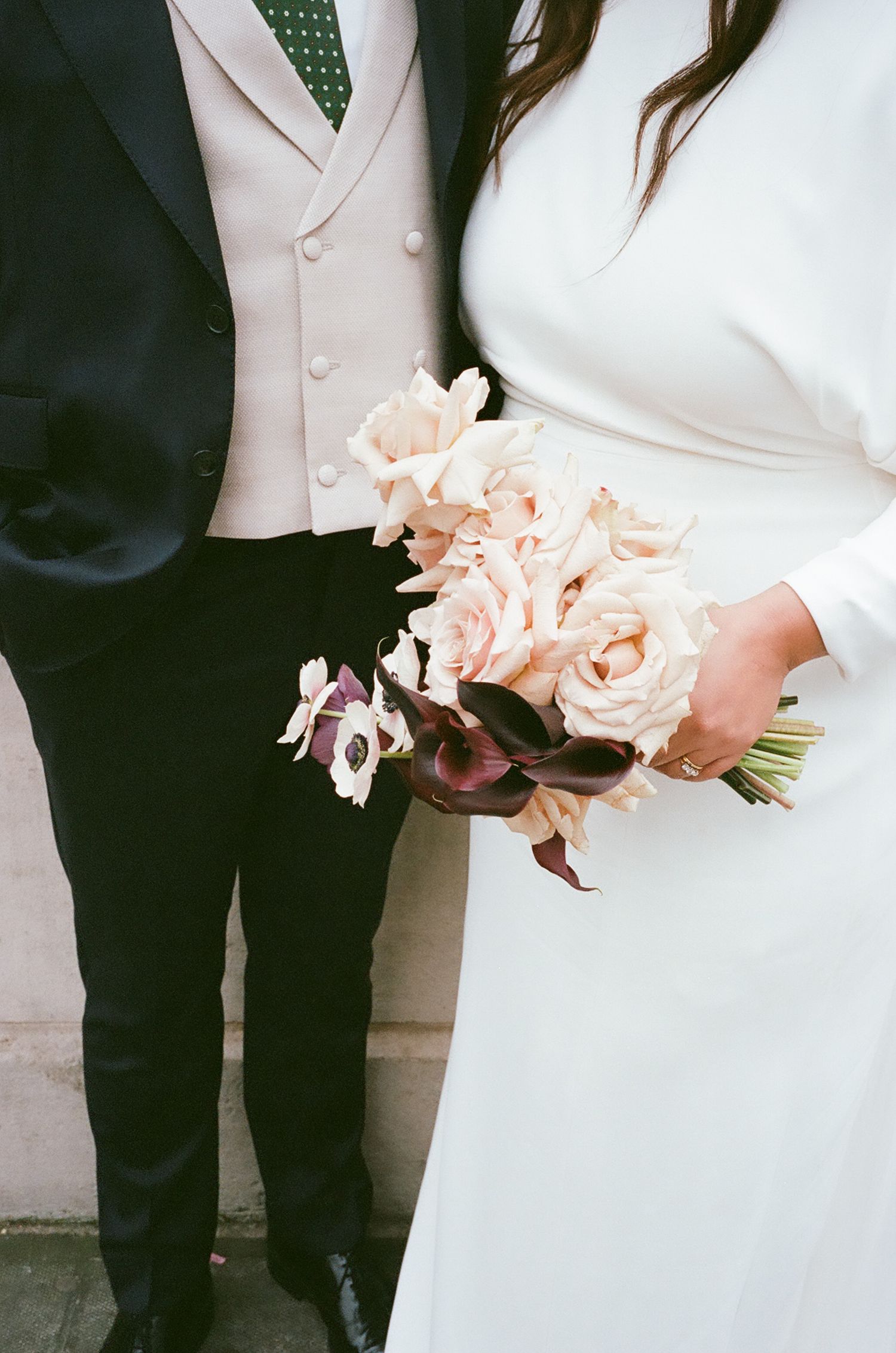 Wedding couple in black and white attire holding peach-colored floral bouquets against a light background.