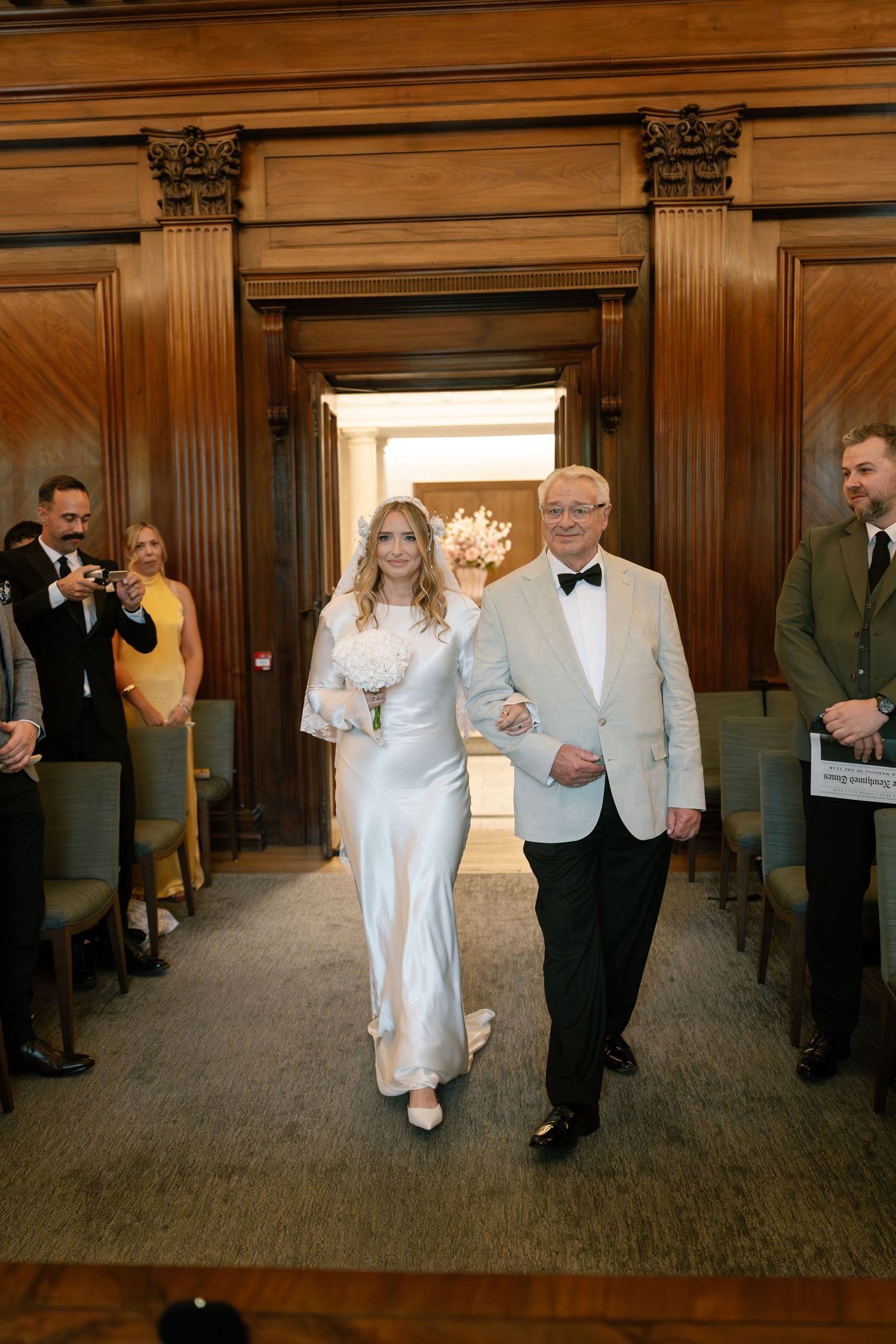 Elegant wedding ceremony in a historic venue with ornate wooden paneling and columns.