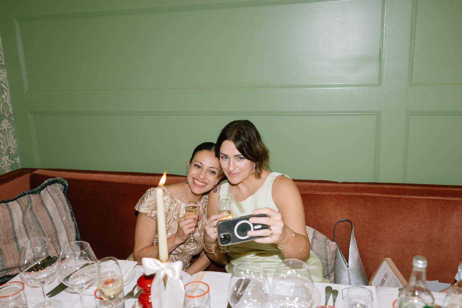 Wedding guests enjoying themselves at reception tables with a green wall backdrop.