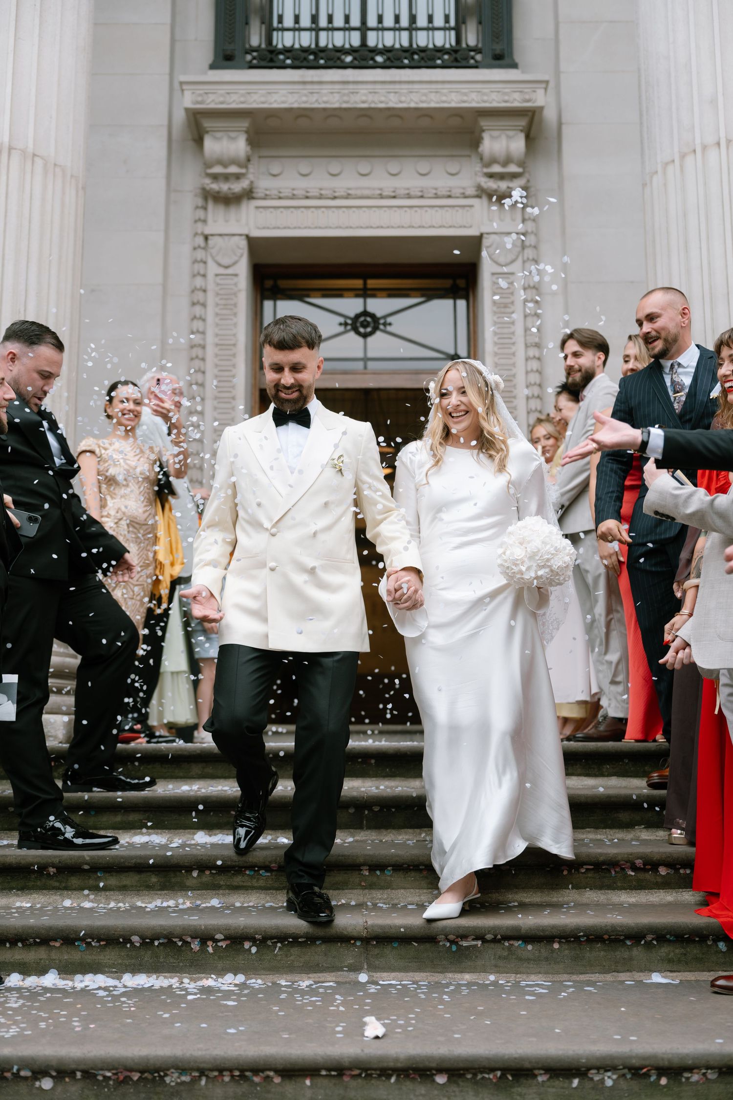 Wedding celebration with confetti outside a grand building entrance.
