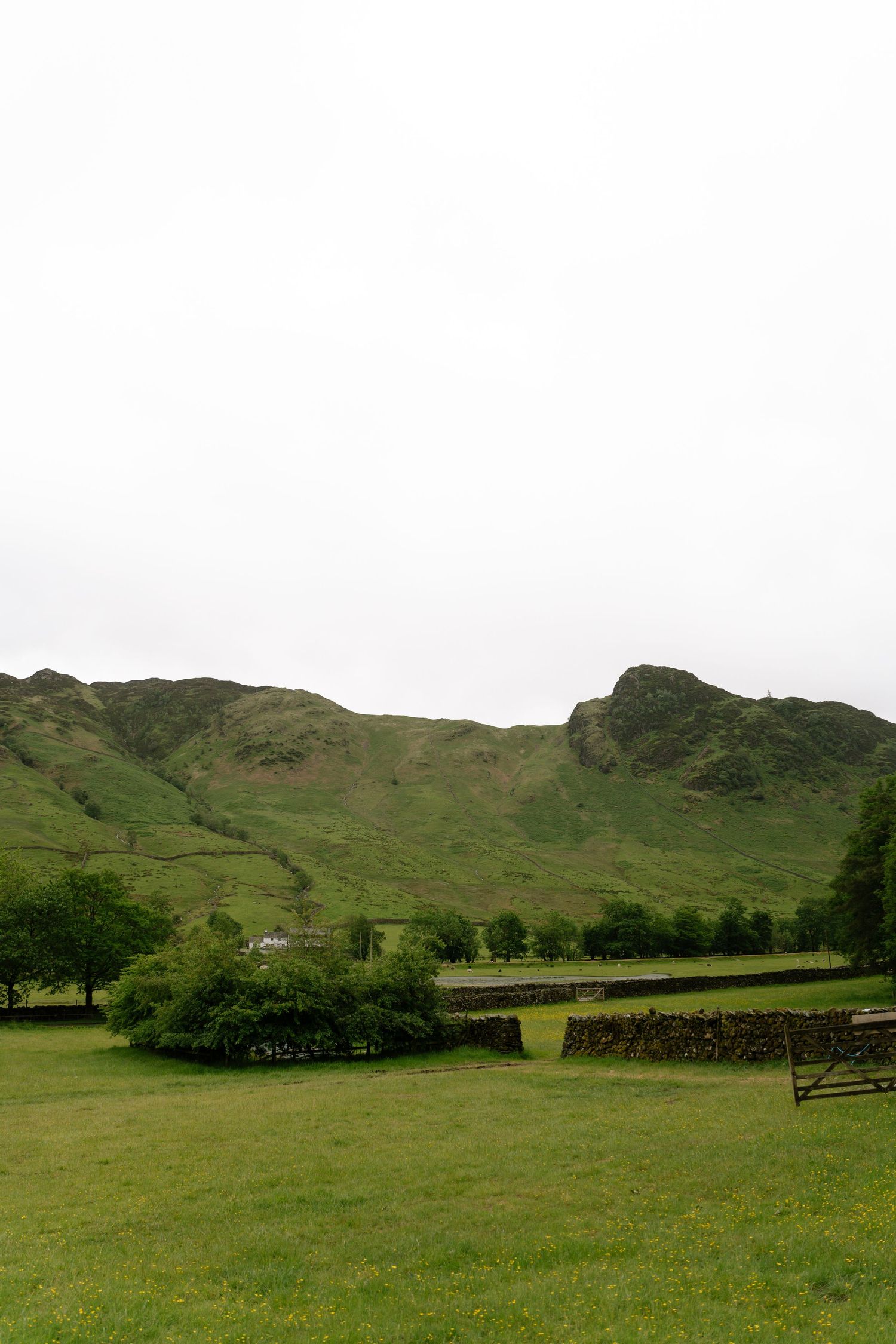 Rolling green hills and mountains stretch across a pastoral landscape with stone walls and scattered trees.