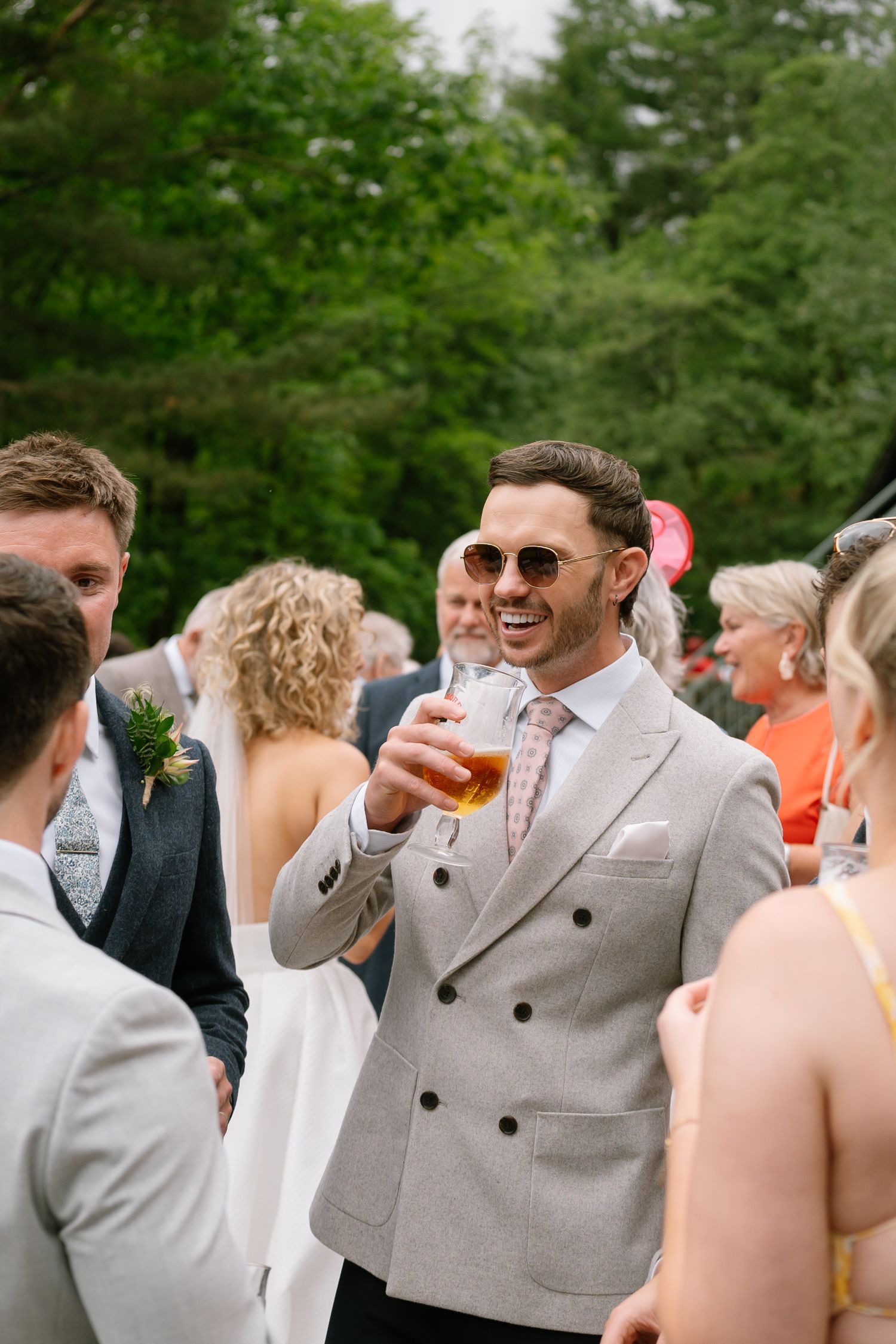 Wedding celebration outdoors with guests mingling and enjoying drinks in summer attire.