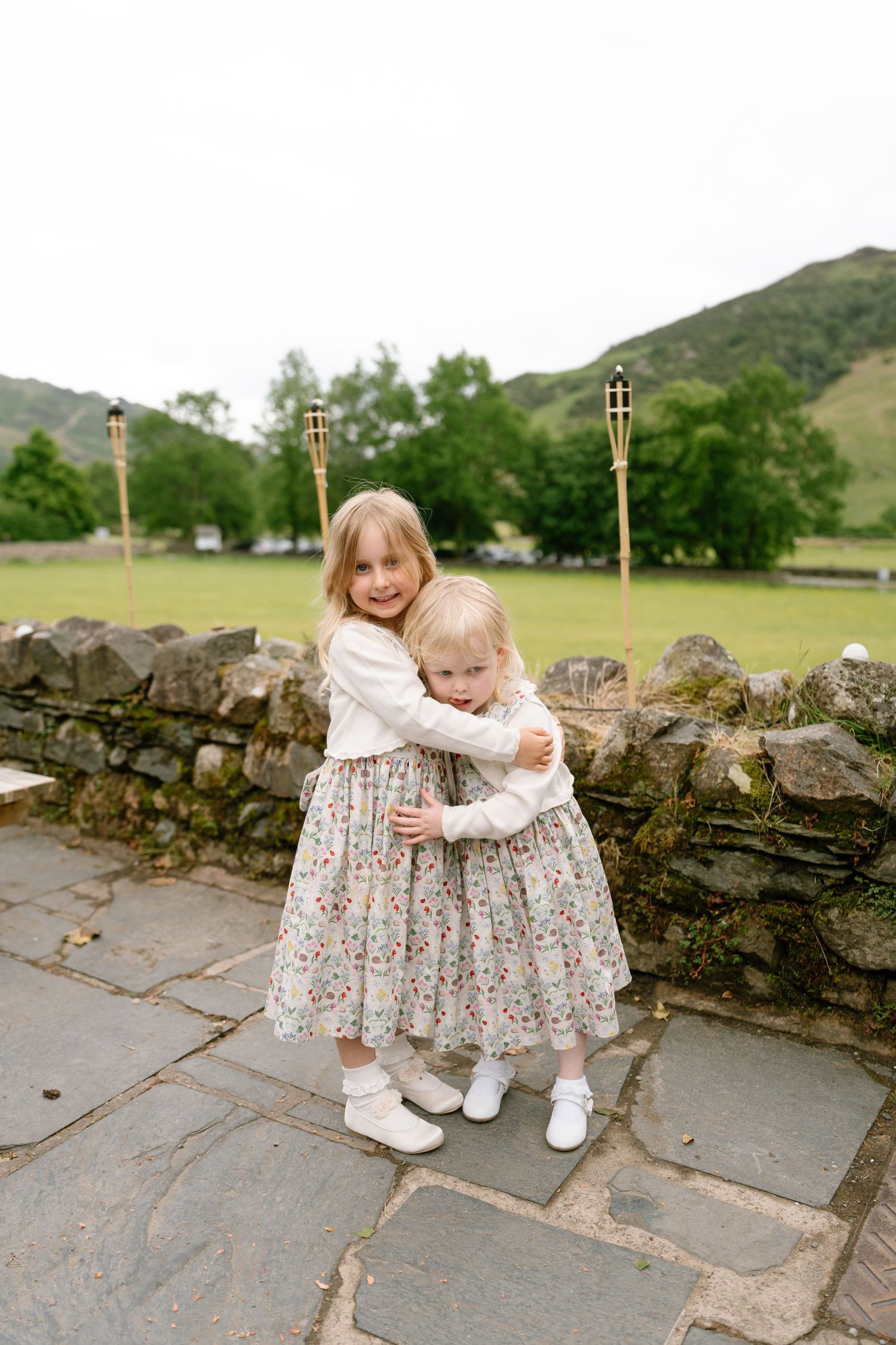 Two young children in floral dresses hugging on stone steps outdoors.