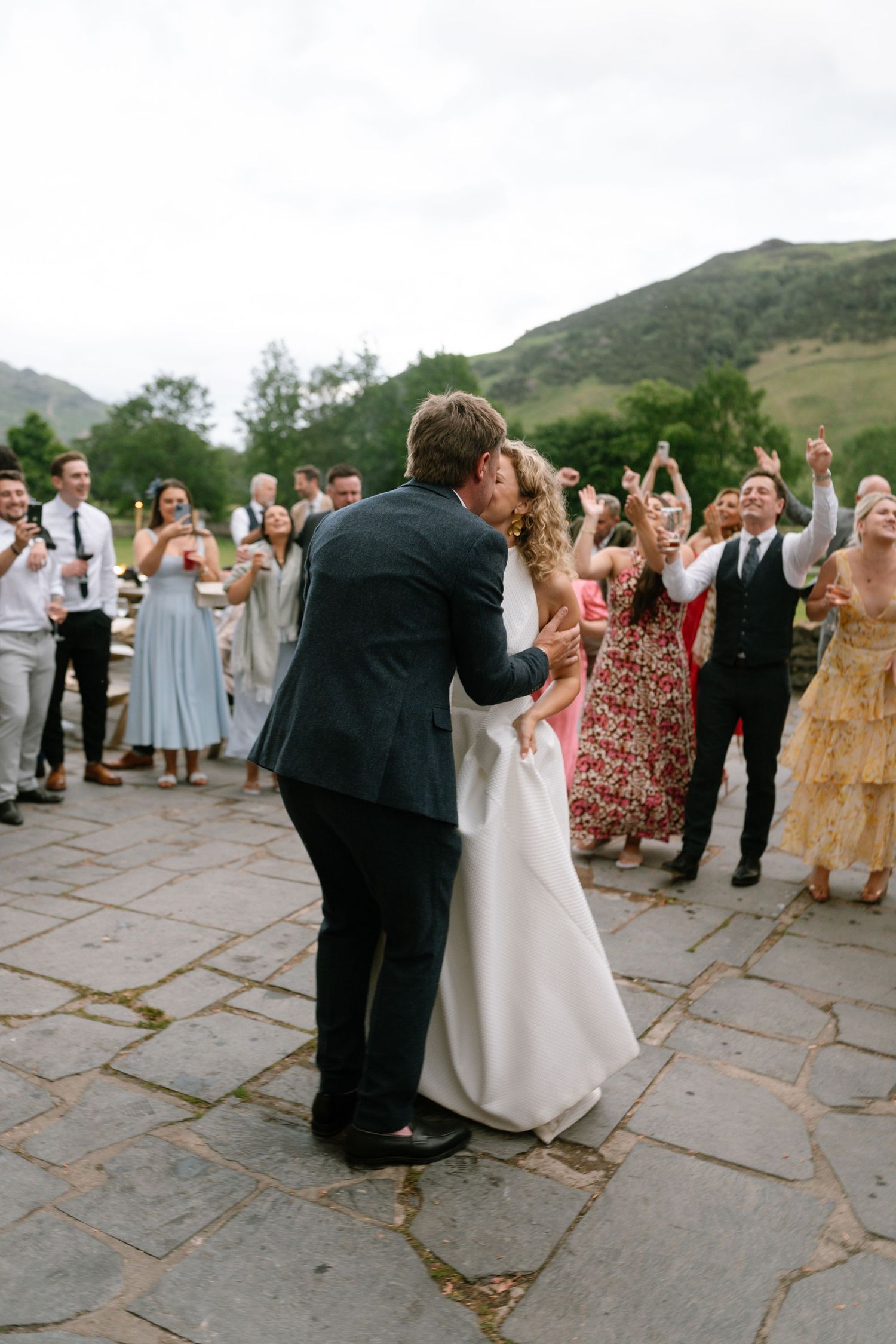 Wedding party and guests celebrating with joyful dance moves on outdoor stone patio.