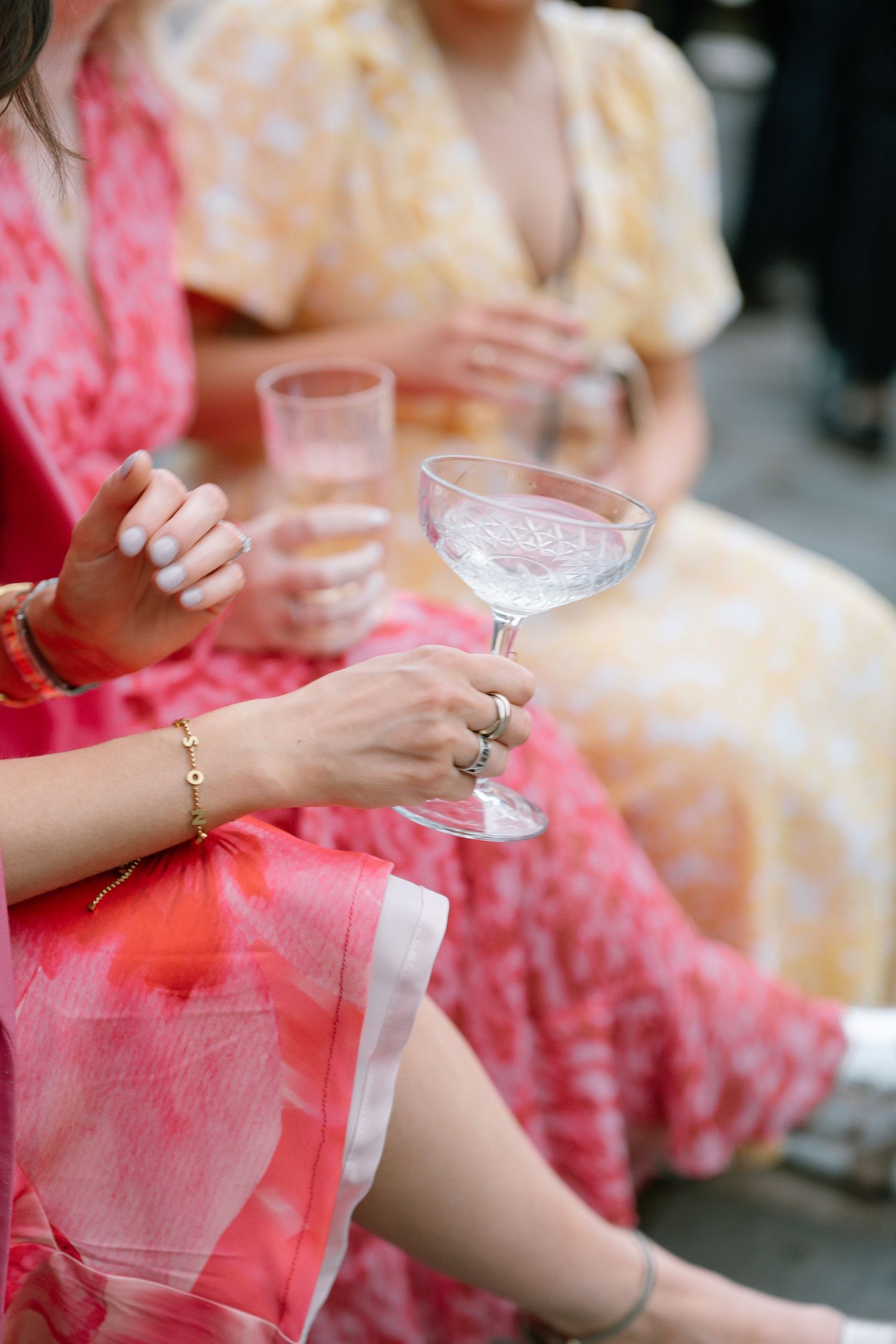 People holding cocktail glasses in formal attire with coral and pink dresses.