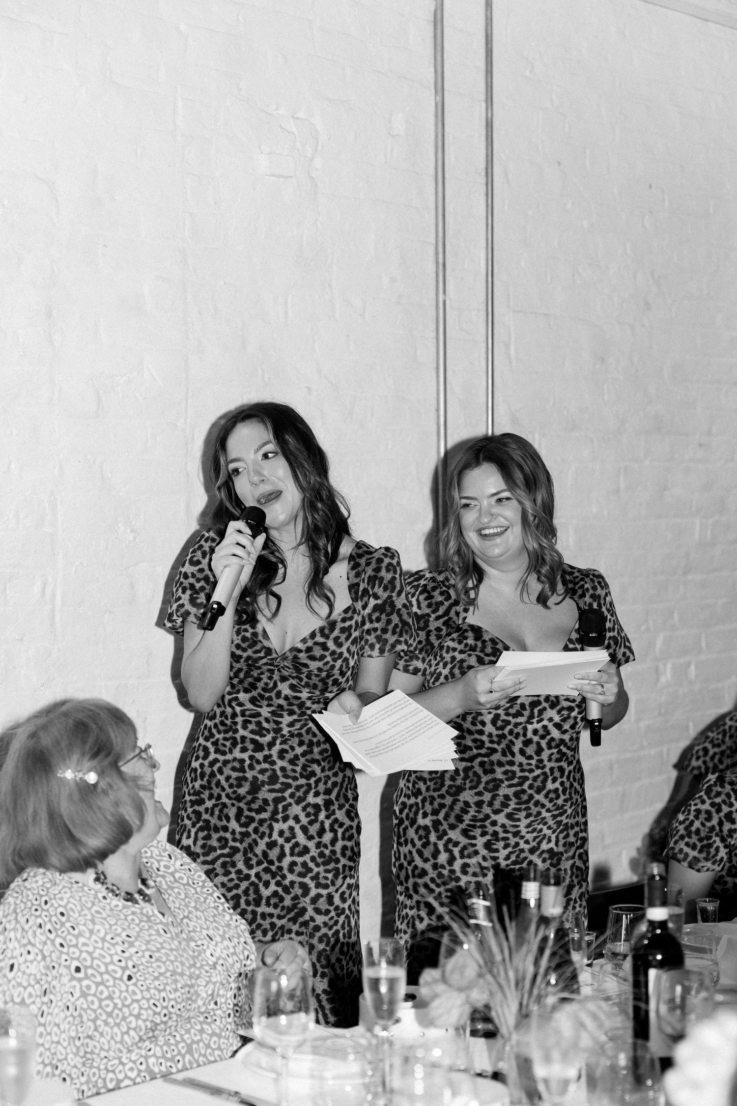 Bridesmaids in matching animal print dresses laugh together at wedding reception dinner.