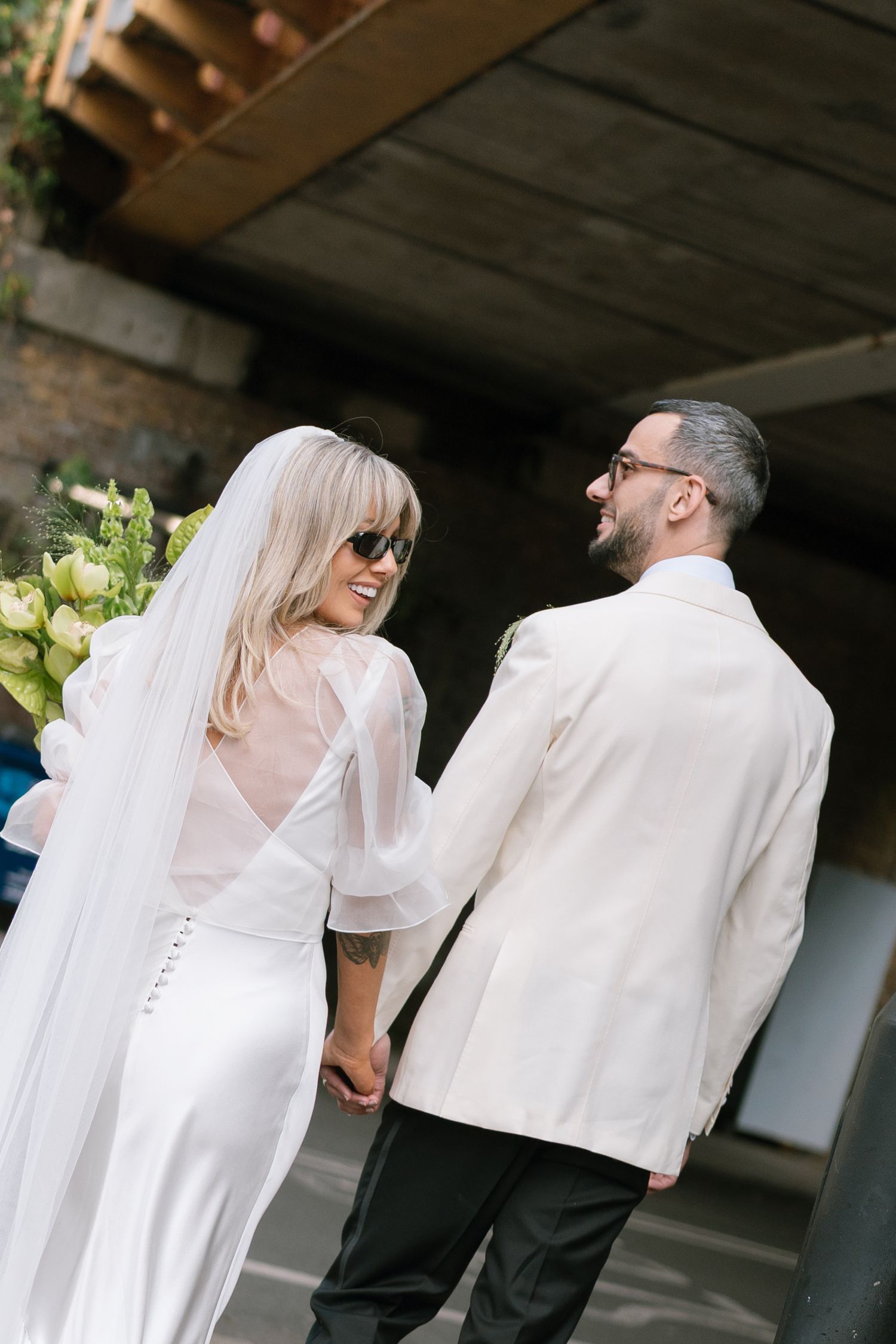 Wedding couple in white attire poses together in urban setting.
