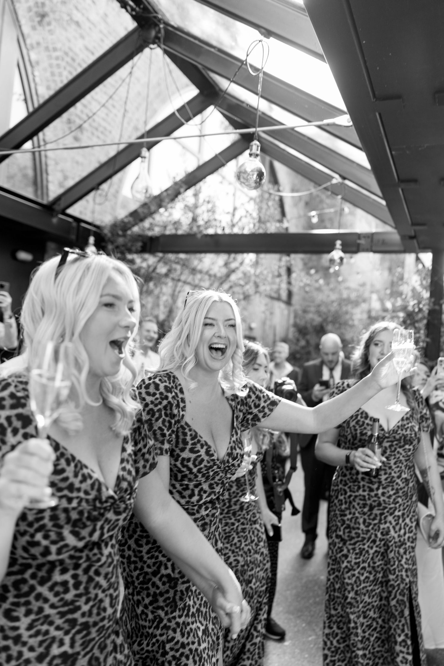 Wedding guests in leopard print dresses celebrate joyfully under a clear tent ceiling.