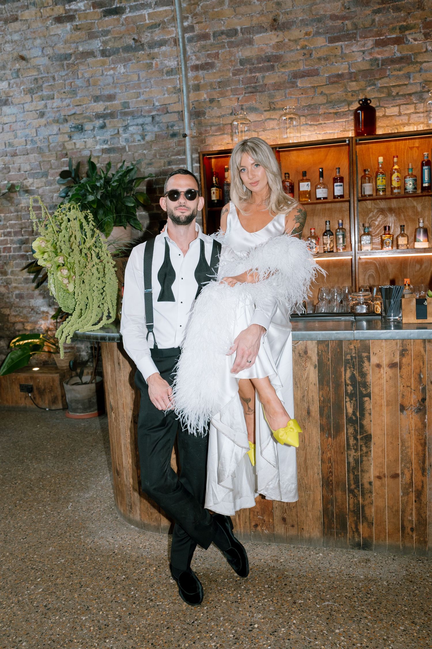 Wedding couple dancing playfully by a rustic wooden bar with exposed brick walls.