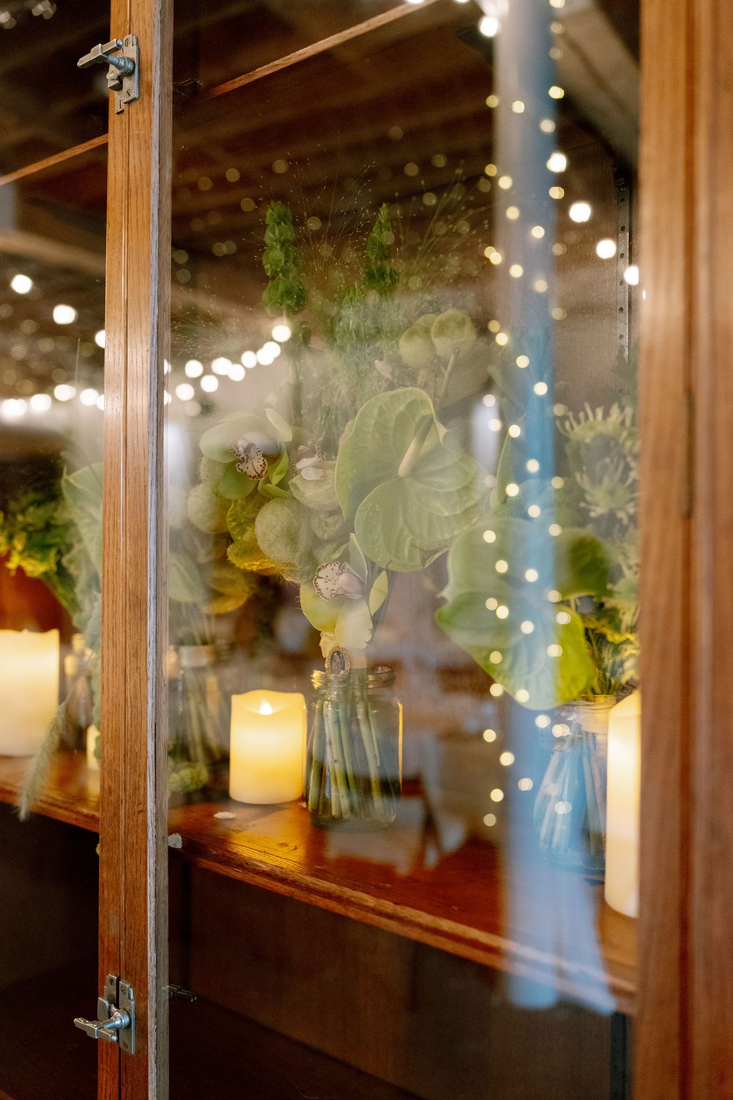Romantic wedding reception decor with string lights and candles glowing through glass windows.