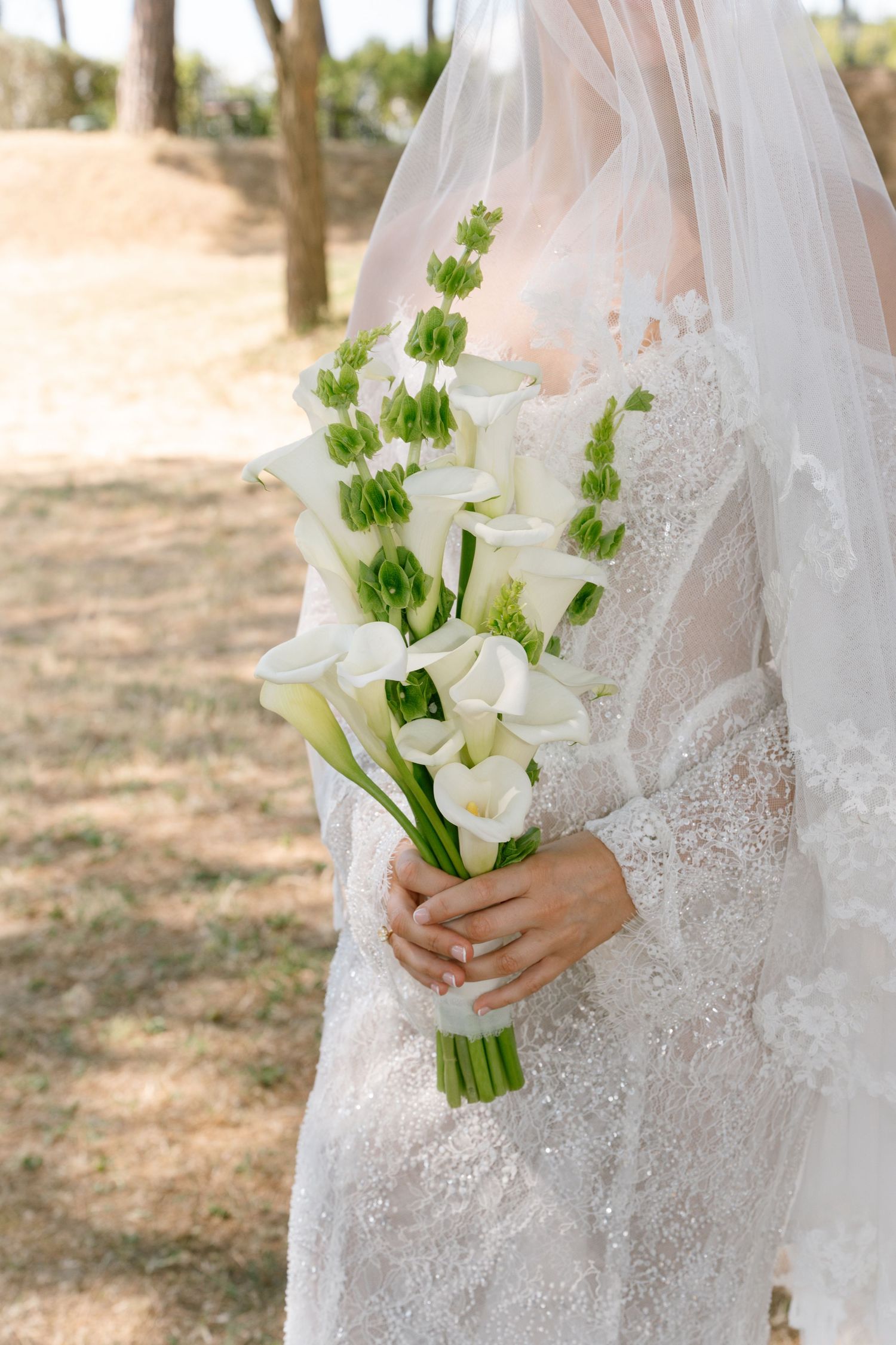 Elegant bridal bouquet featuring white calla lilies and green accents against a lace wedding dress.