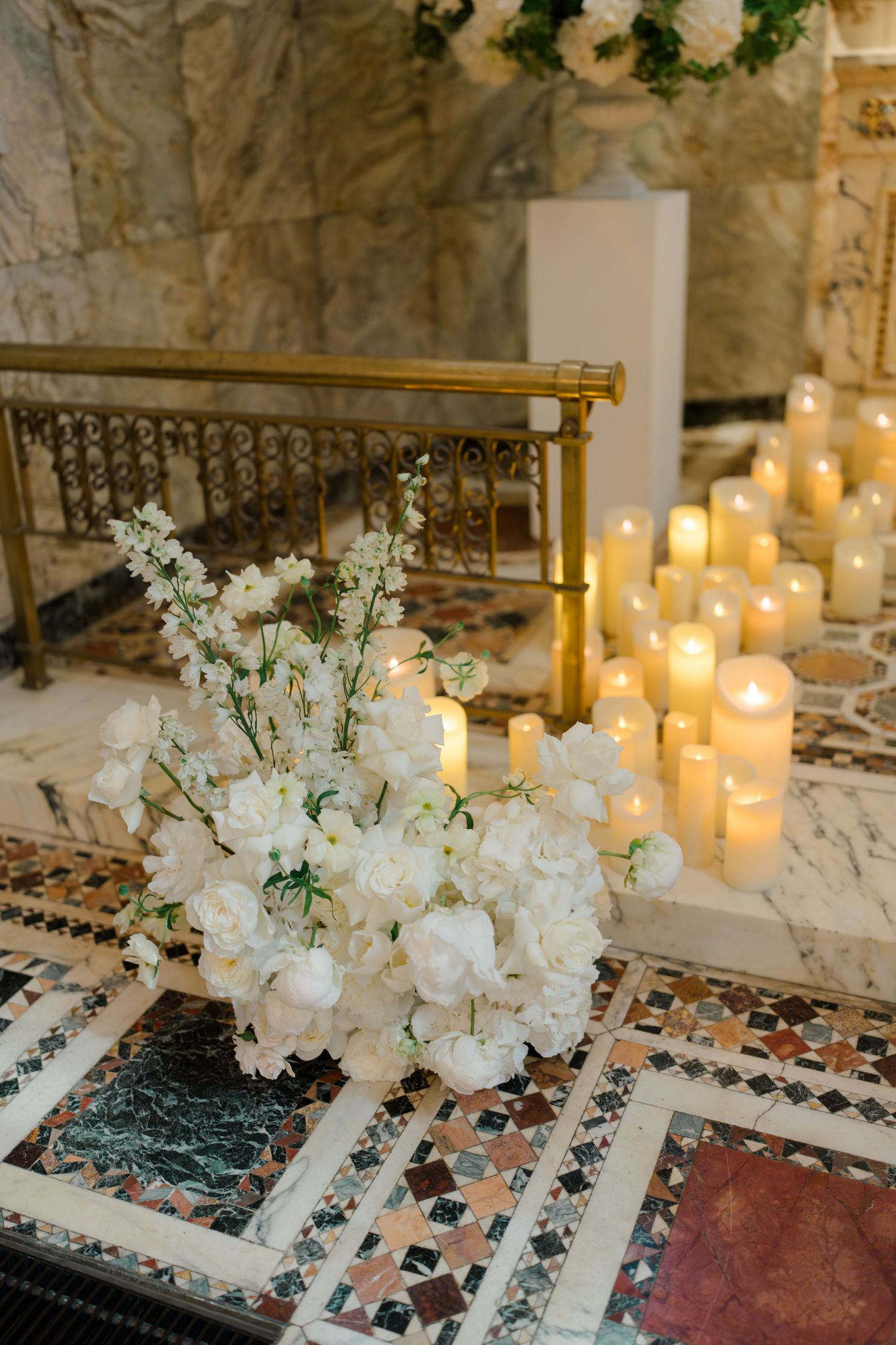 White floral arrangement with cherry blossoms beside glowing pillar candles on ornate mosaic floor at wedding venue.