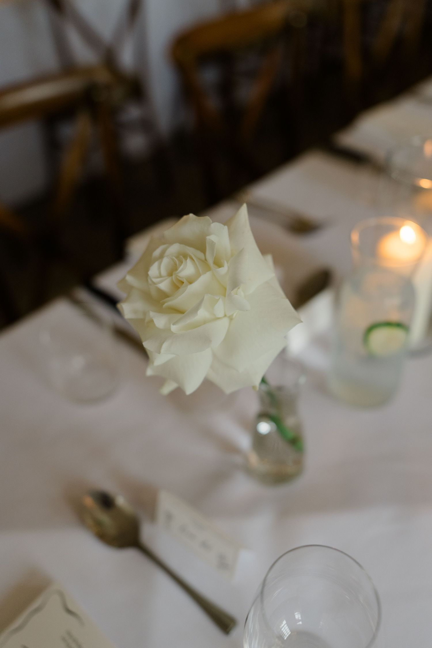 Elegant white rose centerpiece with candle on a white linen wedding reception table.