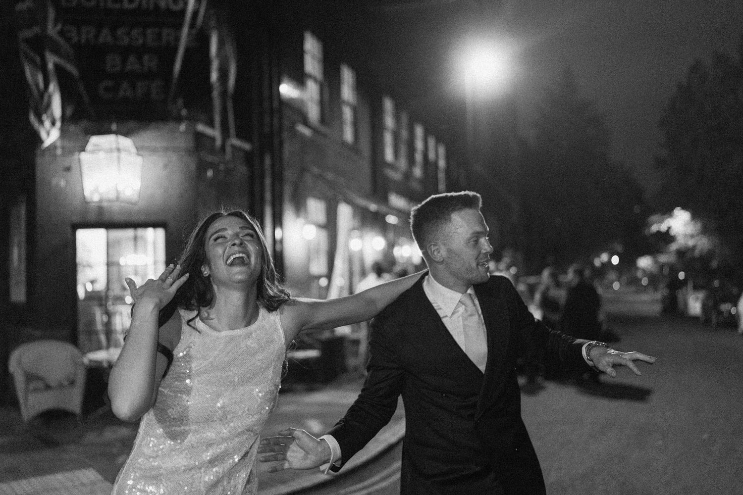 Bride and groom laugh and dance together on a street at night after wedding.