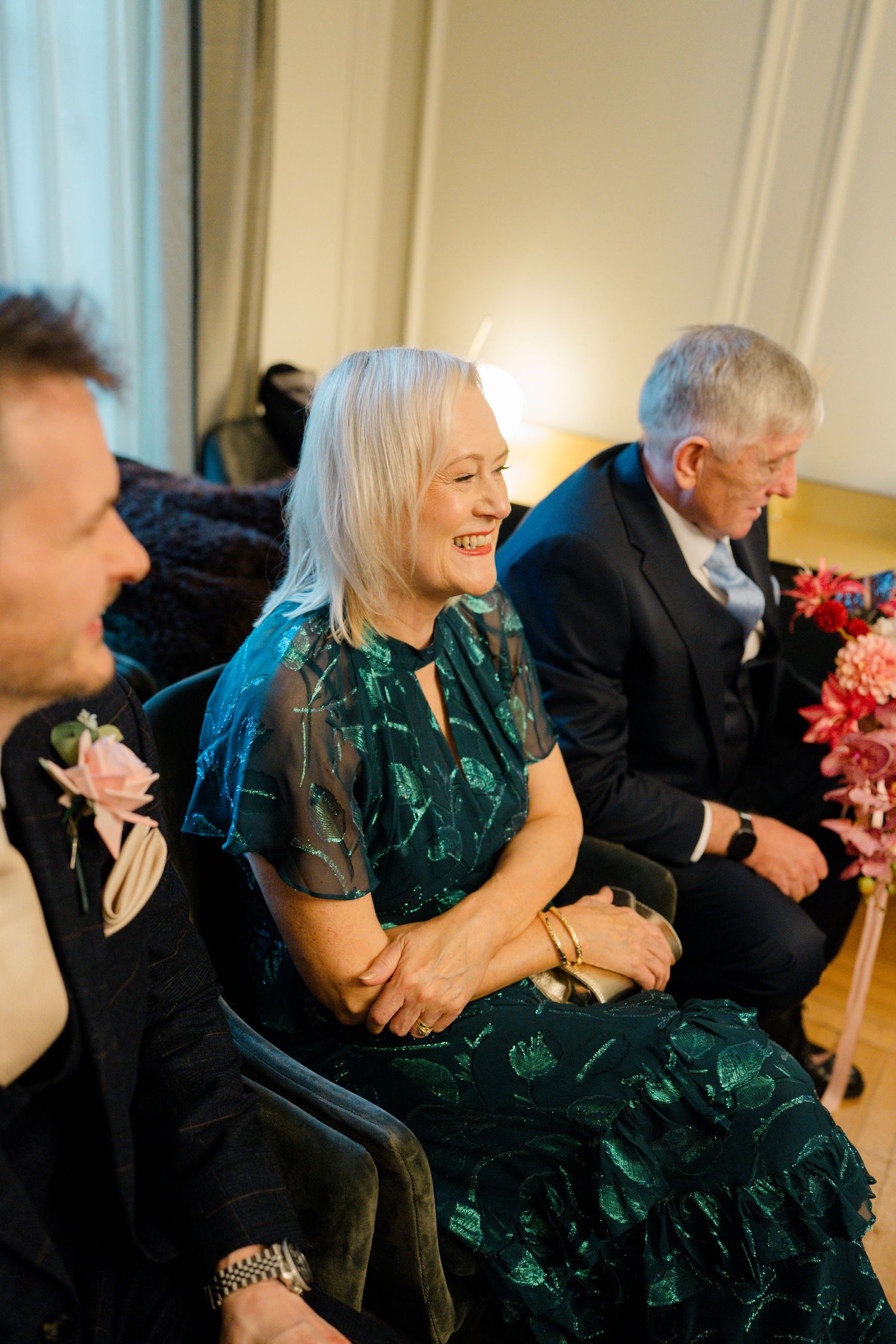Smiling wedding guest in green floral dress seated at intimate ceremony.