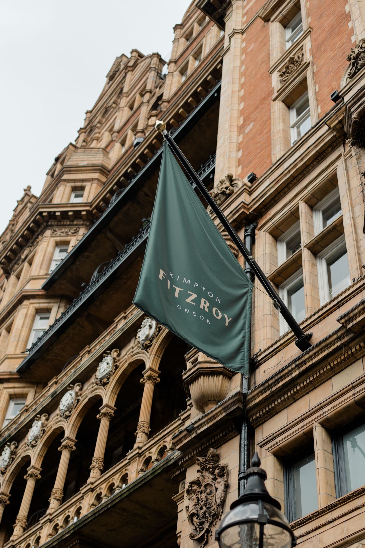 Green Kimpton Fitzroy London hotel flag mounted on ornate Victorian brick building facade.